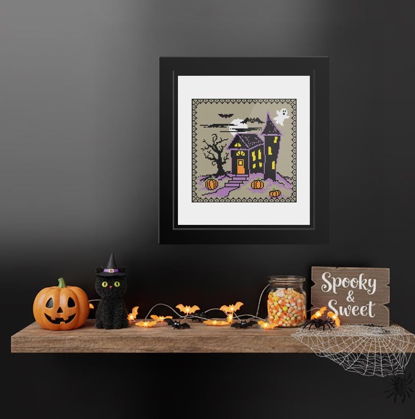 a Halloween-themed display on a shelf, including a framed picture of a spooky house, a carved pumpkin, a witch's hat, a spider web, a jar of candy, and a "Spooky & Sweet" sign.