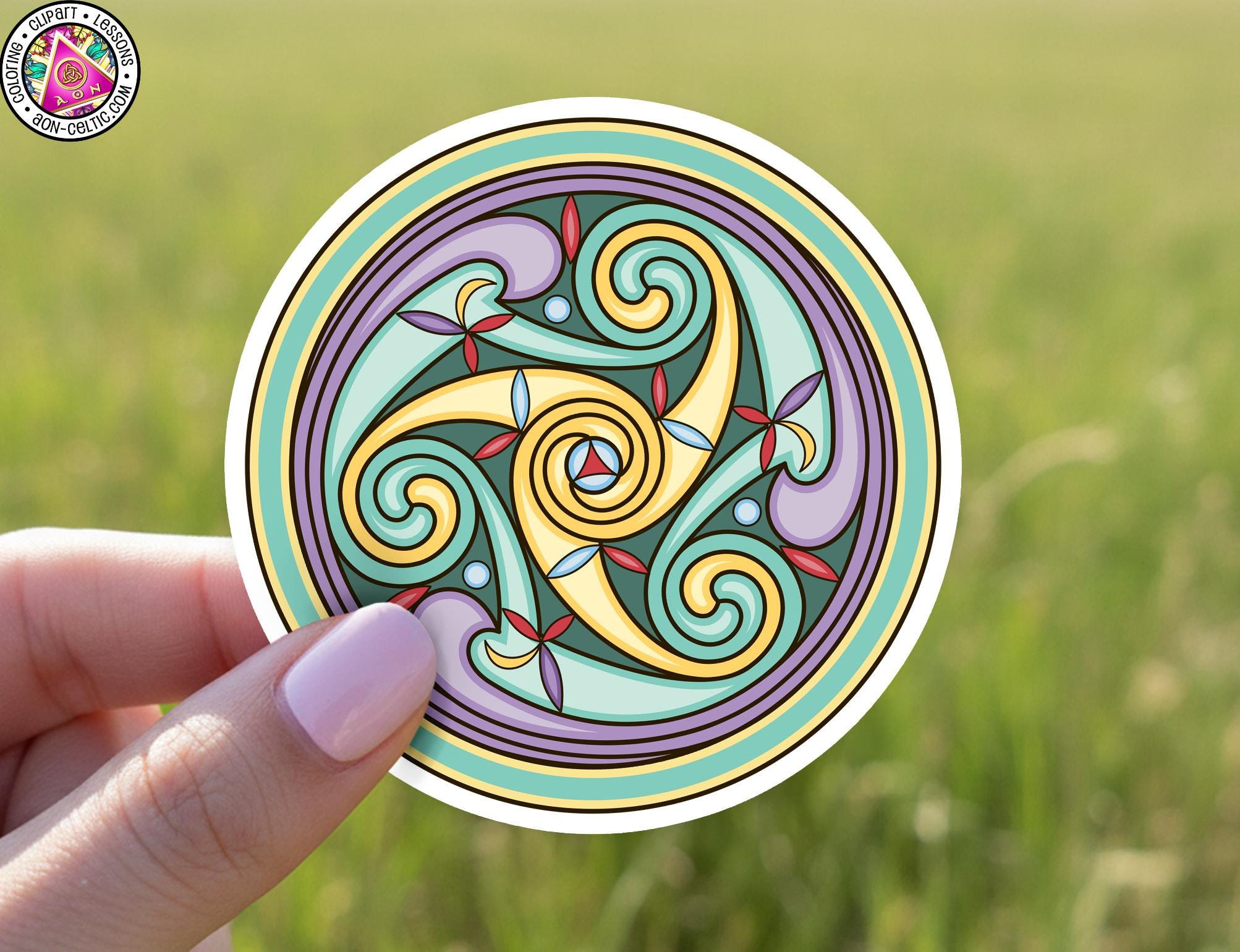 A hand holding a circular sticker with a colorful, swirling design in shades of green, purple, yellow, and red.