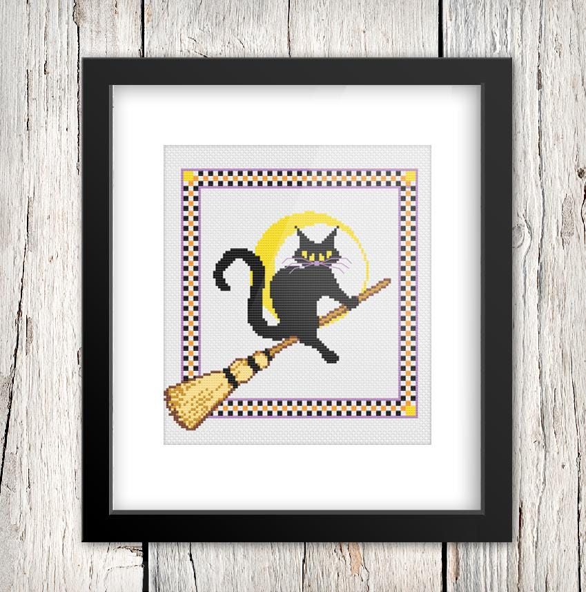A framed cross-stitch image depicting a black cat riding a broomstick.
