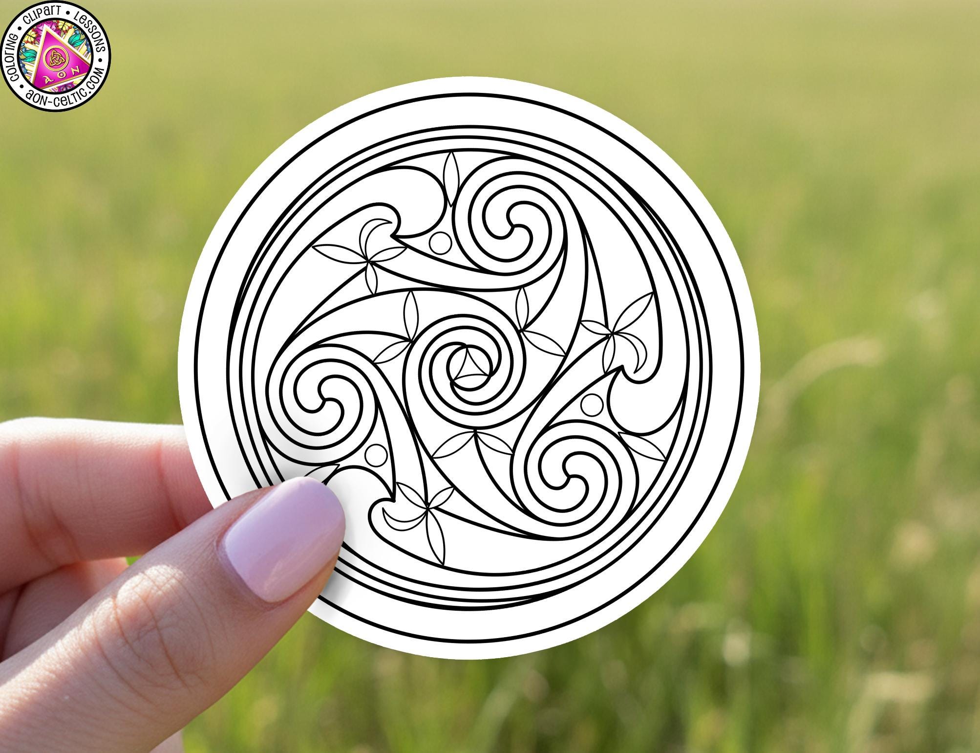 A hand holding a circular sticker with an intricate black and white design featuring swirling patterns and floral elements.