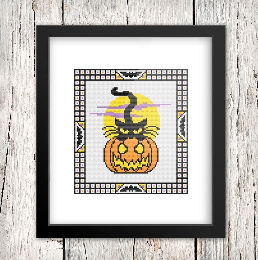 A framed cross-stitch image depicting a black cat sitting on top of a jack-o-lantern.