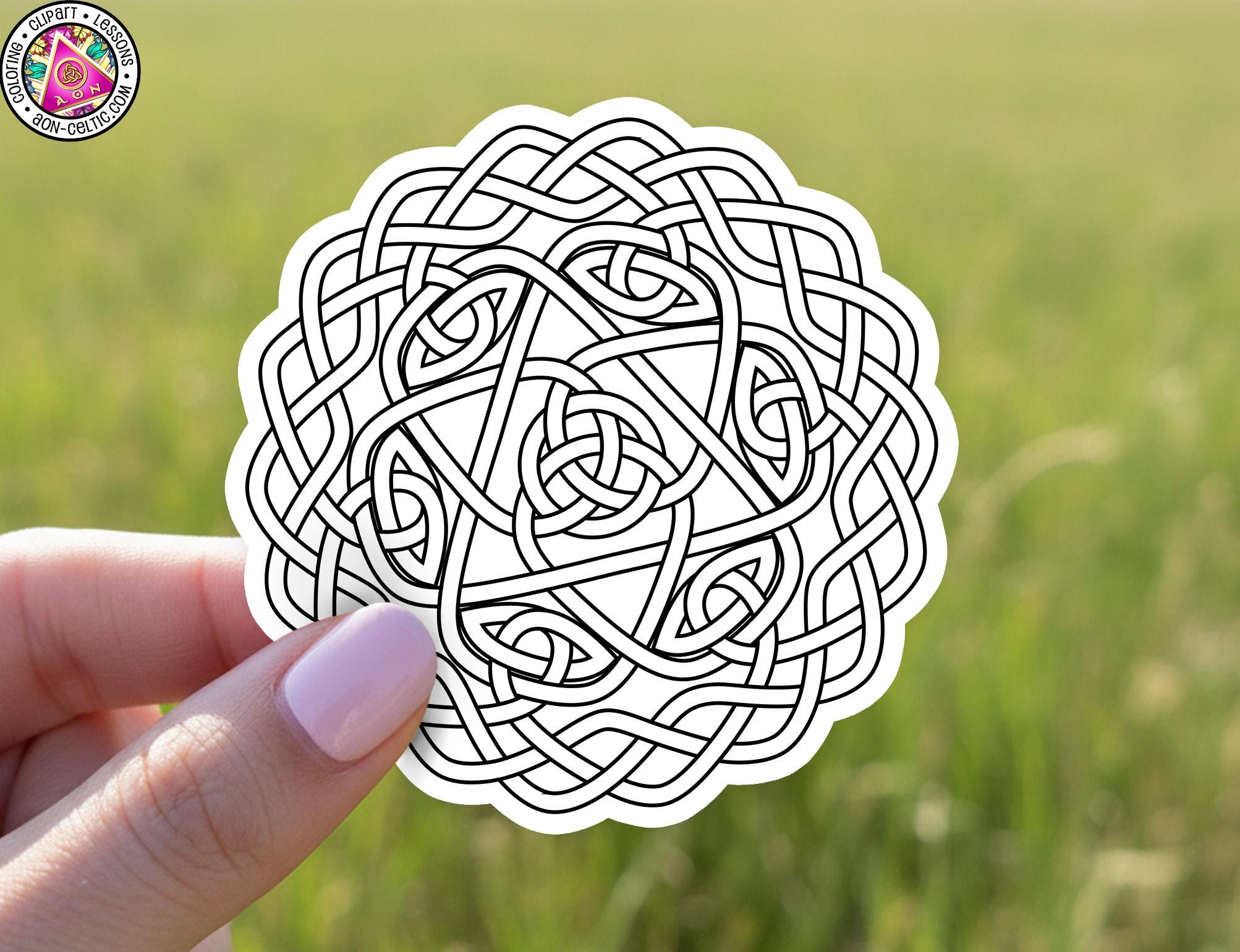 A hand holding a circular sticker with a complex, intricate Celtic knot design.