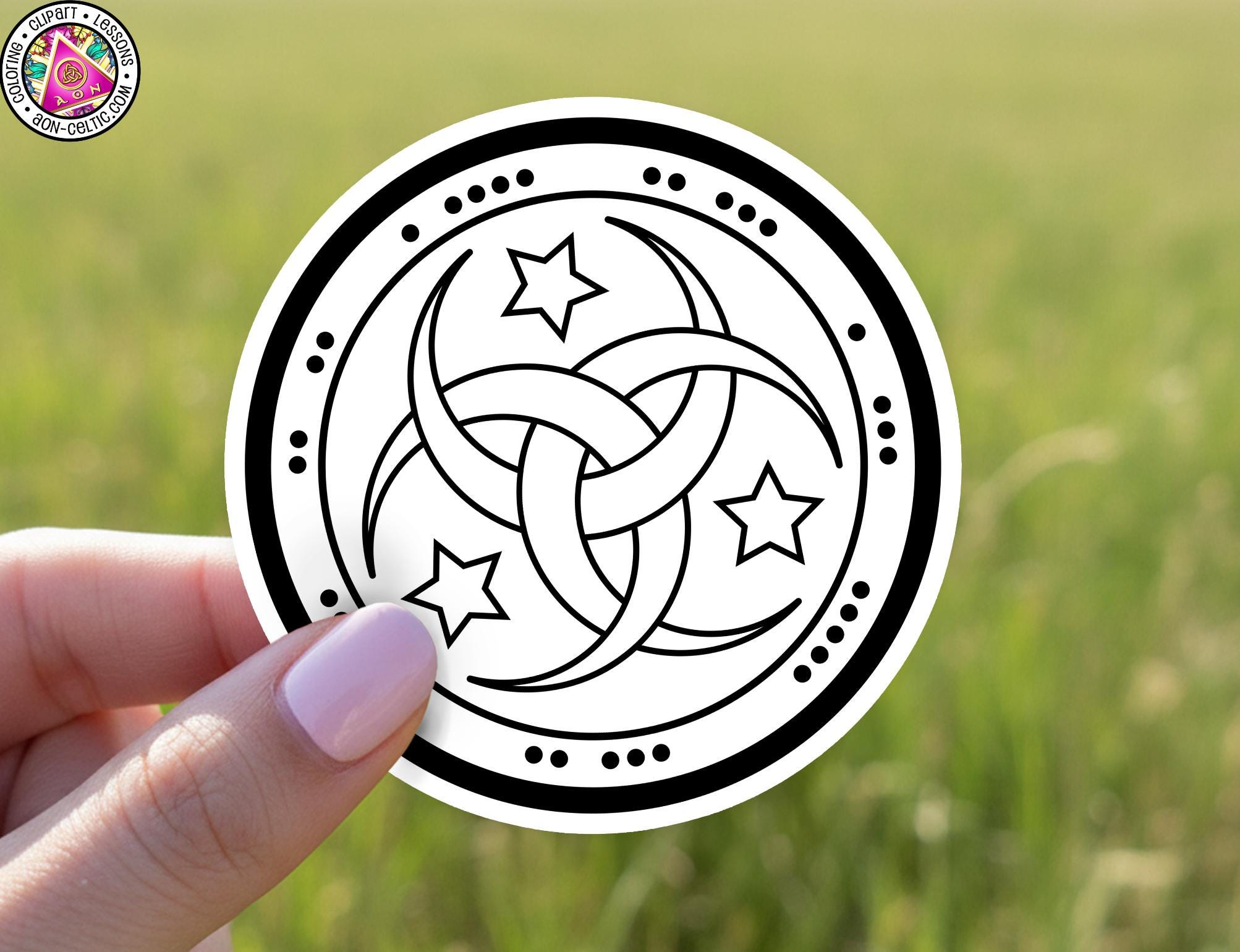 A hand holding a circular sticker with a black and white design featuring stars and crescent moons.