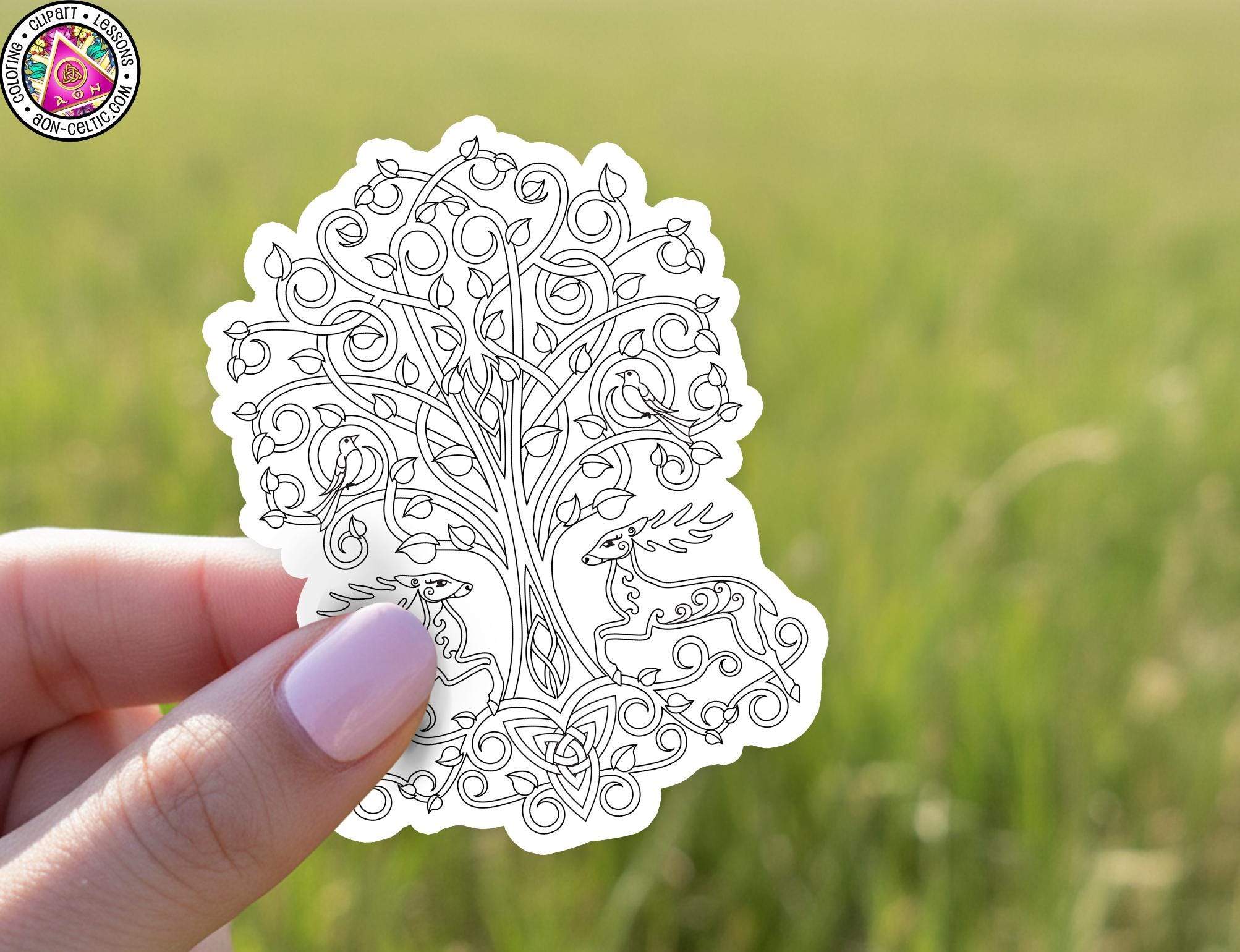 A hand holding a white sticker with a detailed black and white illustration of a tree and two deer.