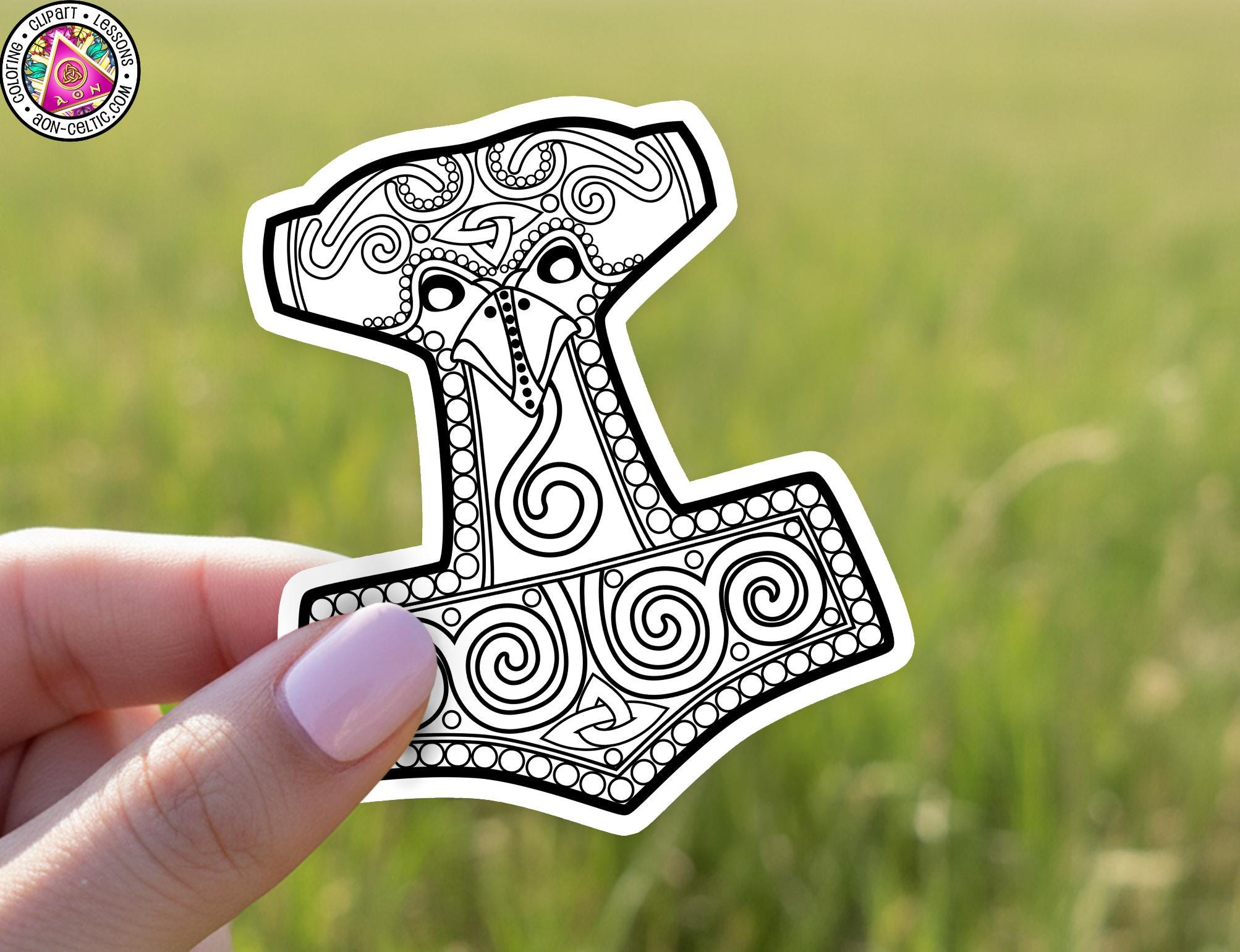 A hand holding a sticker of a stylized hammer or chisel with intricate designs and patterns.