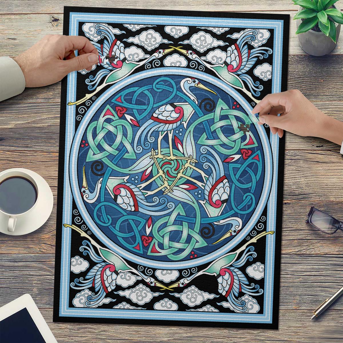 a large, intricate mandala-like artwork with a blue and white color scheme, surrounded by various decorative elements such as birds, swirls, and geometric patterns. The artwork is displayed on a wooden surface, with a cup of coffee and a pair of glasses nearby.