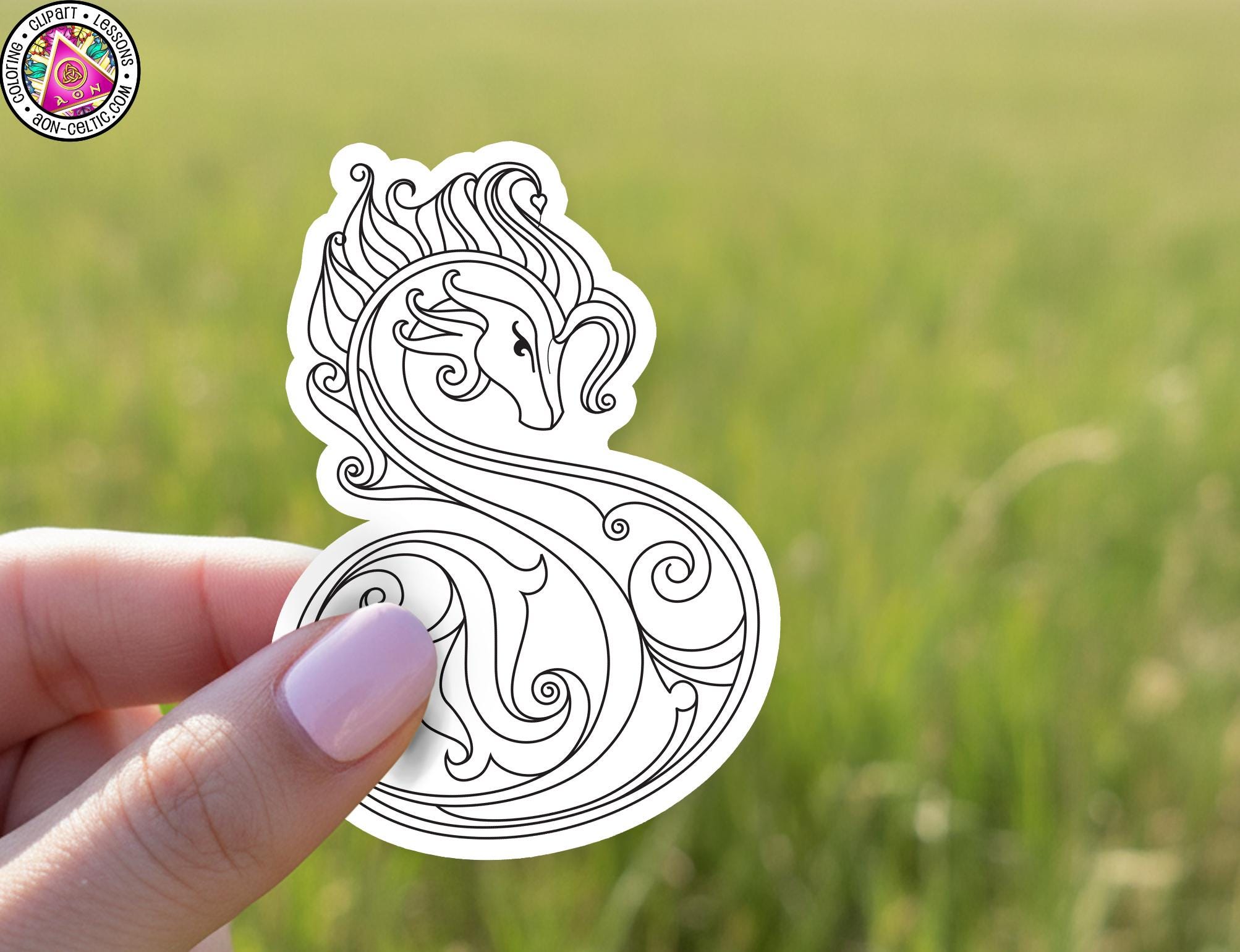 A hand holding a white sticker with an intricate black and white design resembling a stylized letter or symbol.