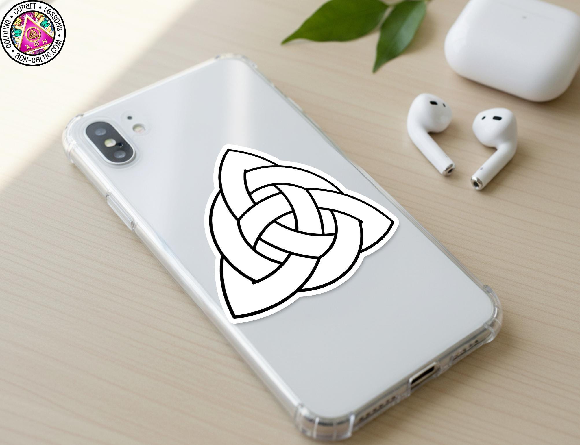 a smartphone with a sticker of a Celtic knot on its back cover, along with a pair of earbuds and a white earbud case on a wooden surface.