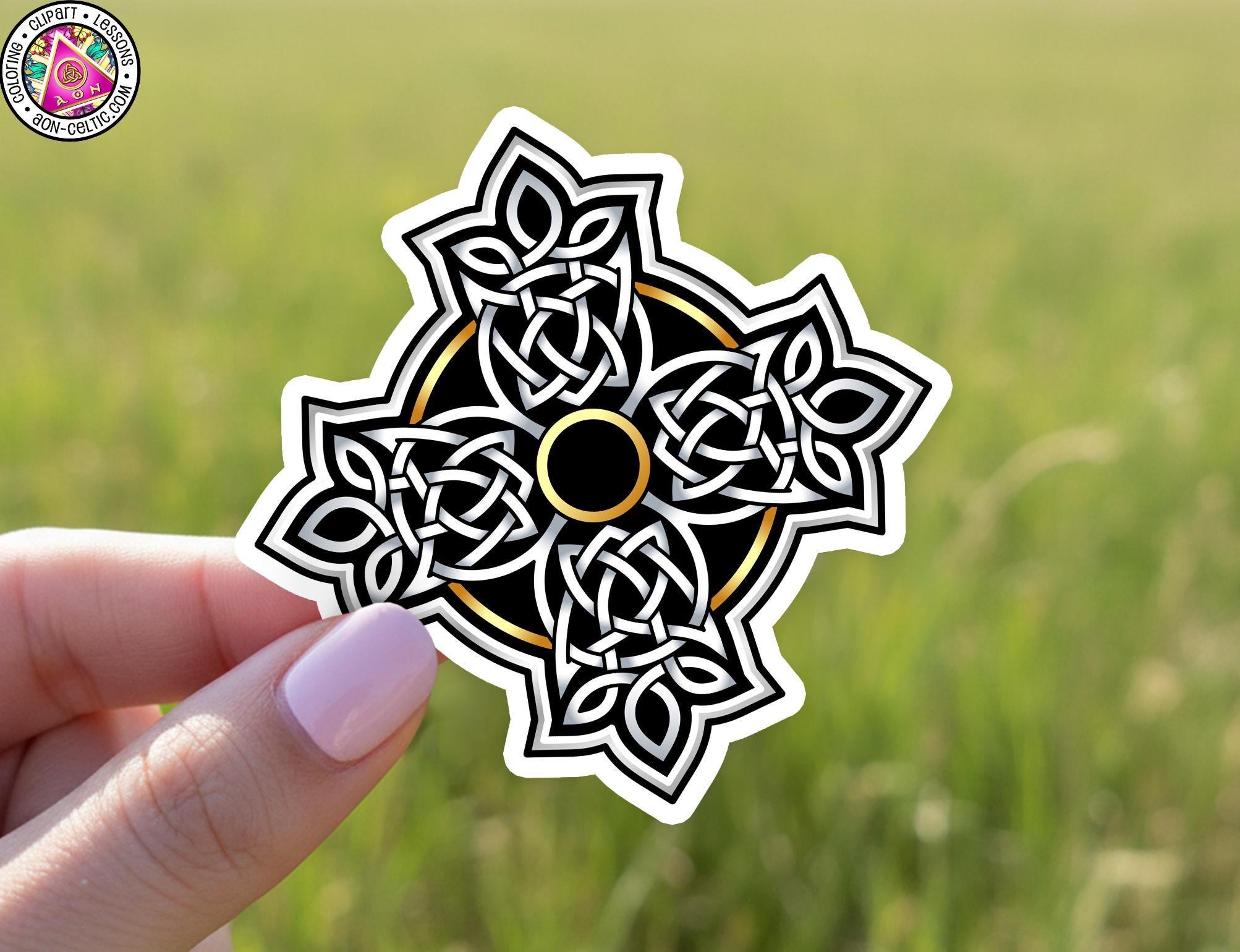 A hand holding a sticker with a decorative design featuring a circular pattern with interlocking lines and shapes.