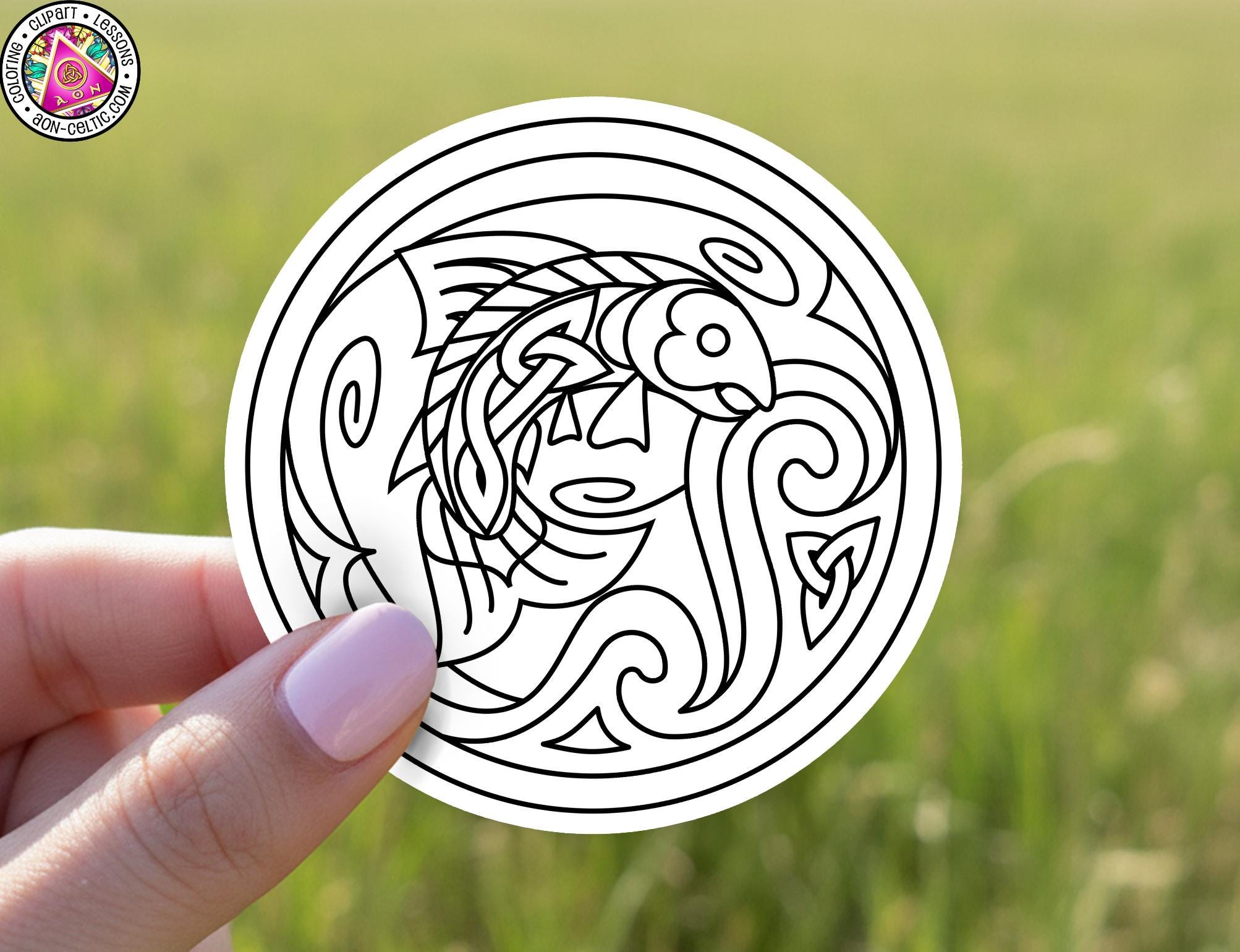 A hand holding a circular sticker with an intricate black and white design featuring a fish and a face.