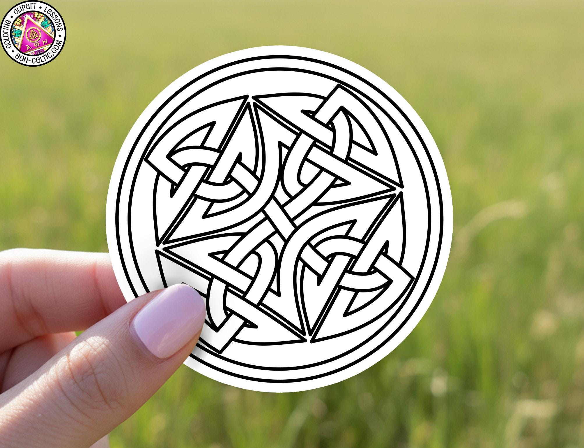 A hand holding a circular sticker with a black and white design featuring a Celtic knot pattern.