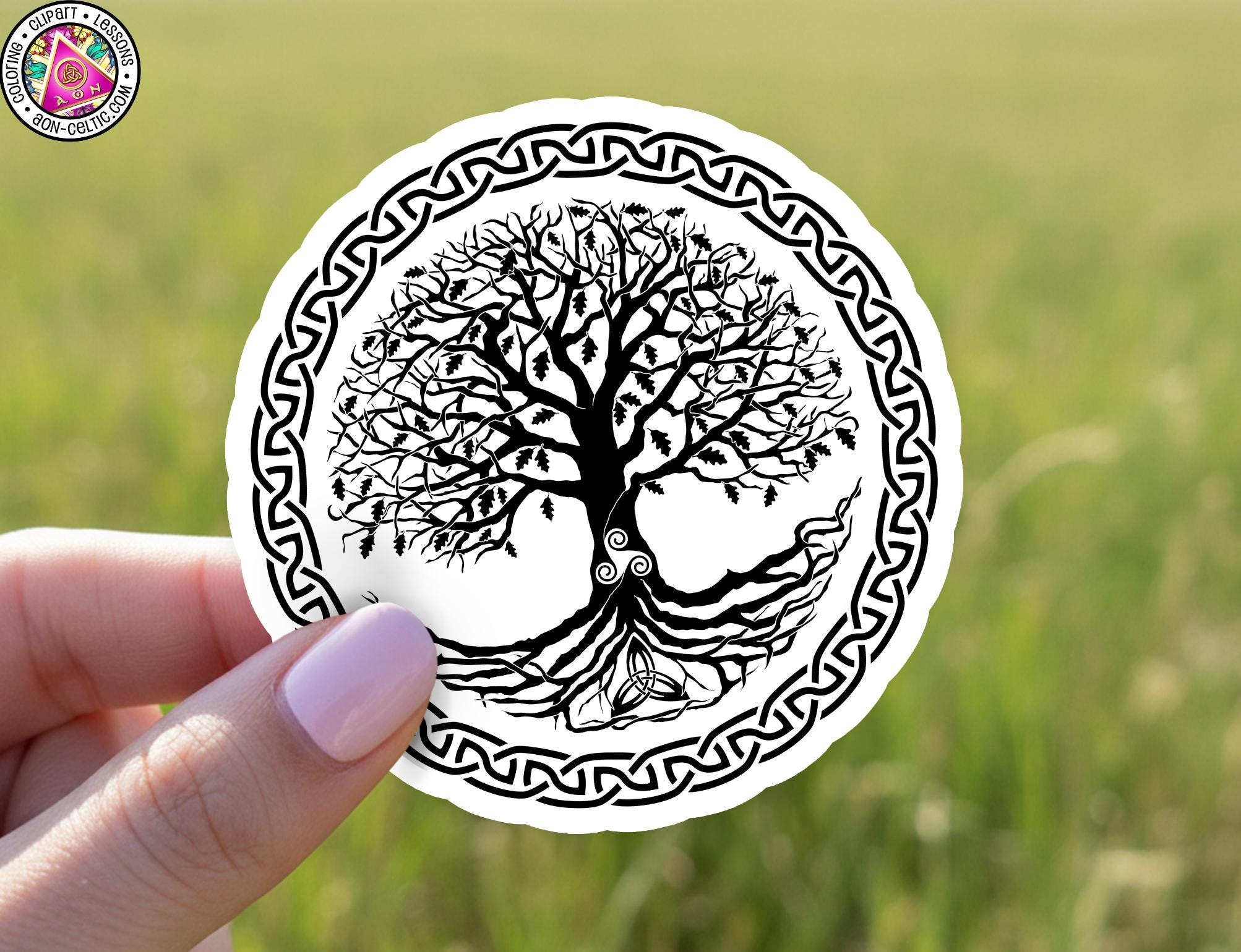 A hand holding a circular sticker with a black and white illustration of a tree with roots and branches, surrounded by a decorative border.