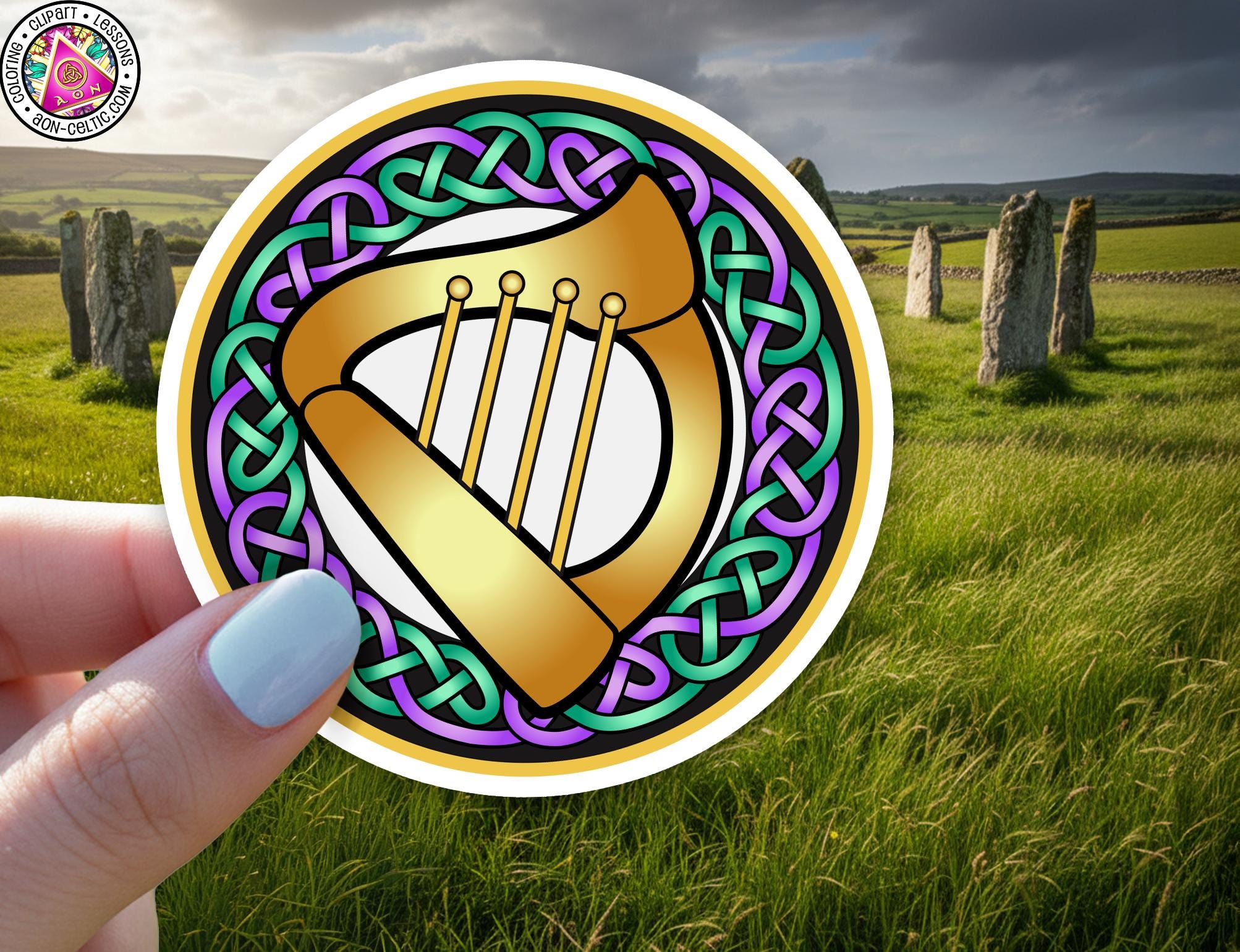 A hand holding a circular sticker with a harp design, set against a background of a grassy field with stone markers.