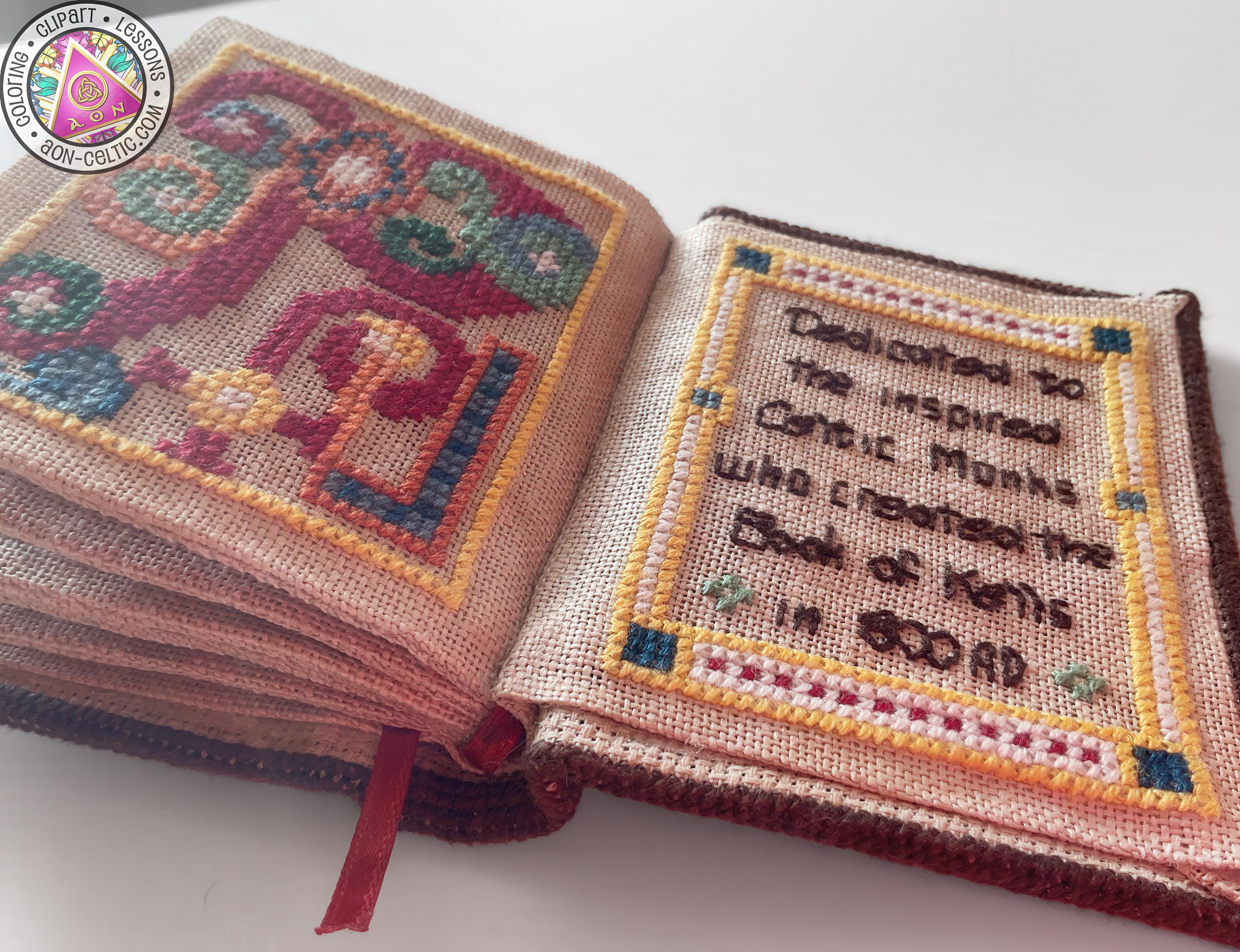 a hand-stitched book with a decorative border, featuring a cross-stitch design and text on the pages.