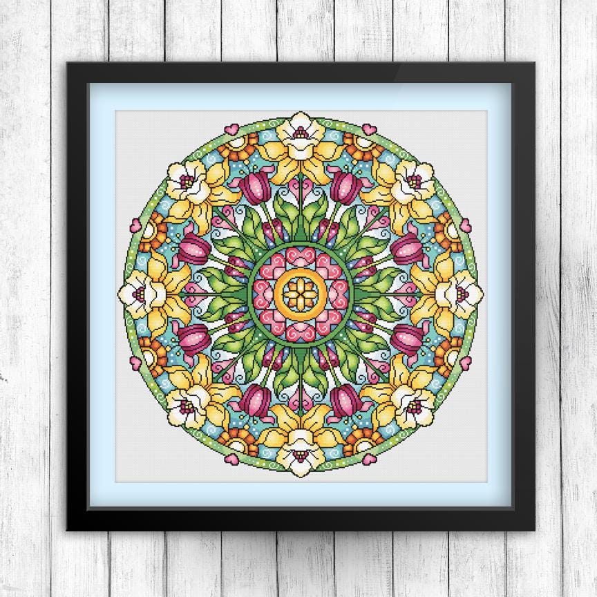 A framed cross-stitch design featuring a vibrant floral pattern with various types of flowers and leaves.