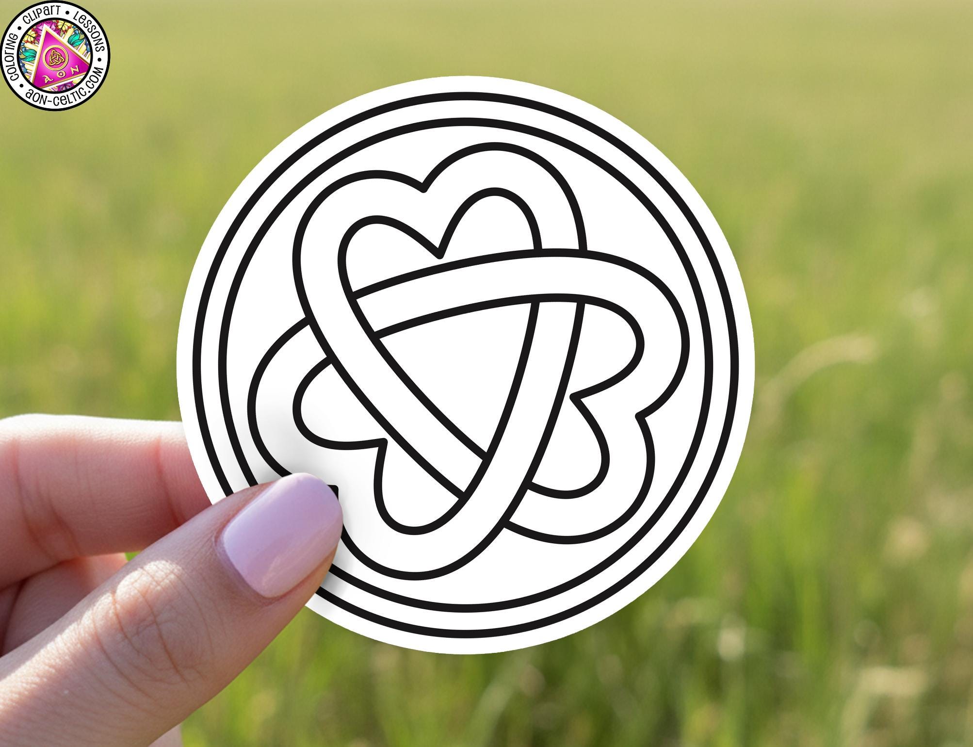 A hand holding a circular sticker with a heart symbol inside it against a blurred green background.