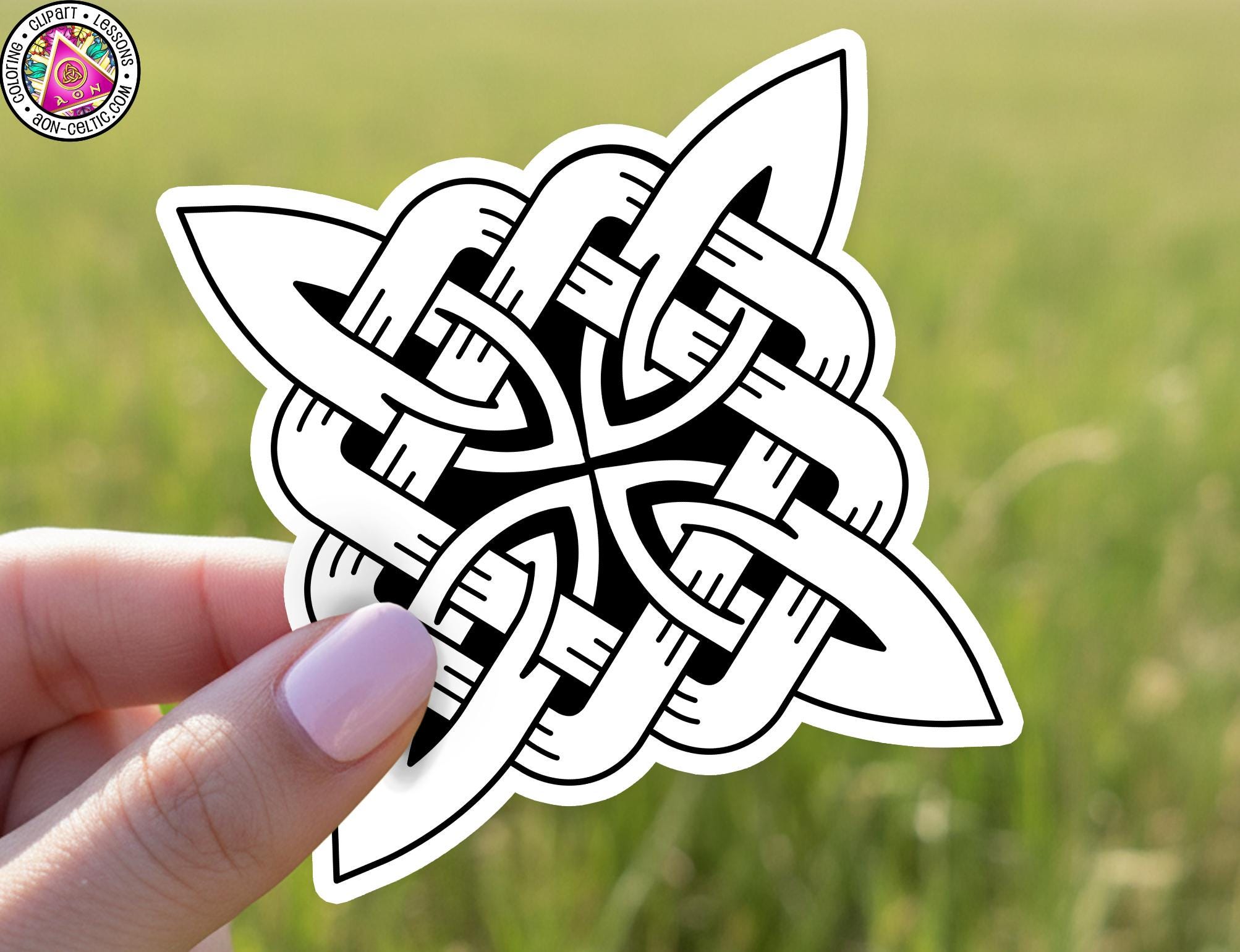 A hand holding a sticker with a black and white design featuring a Celtic knot pattern.
