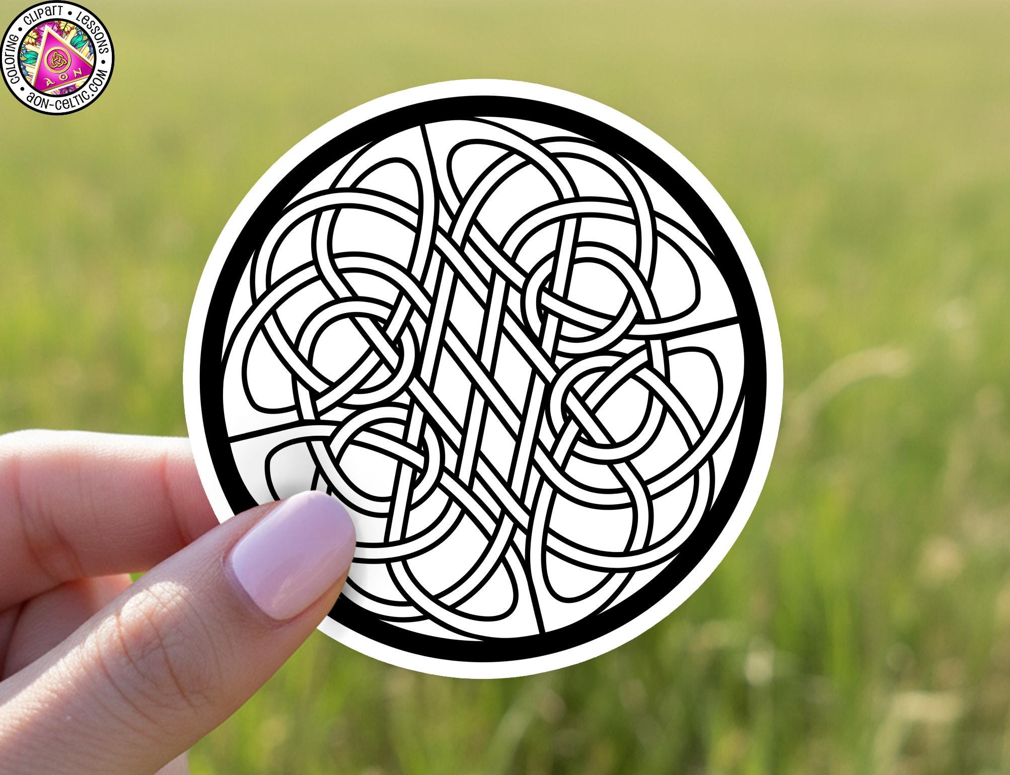 A hand holding a circular sticker with a black and white design featuring a complex, intricate pattern of interlocking lines and shapes.