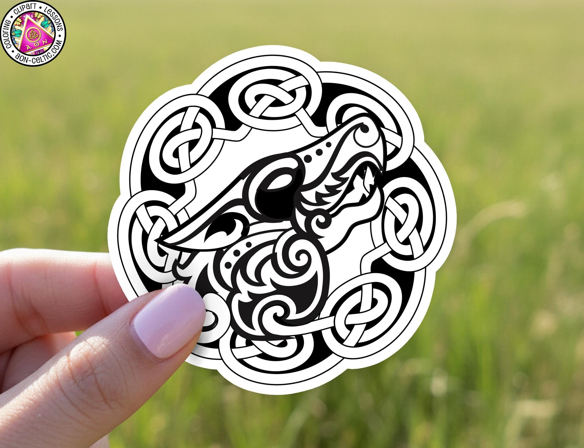 A hand holding a sticker with a black and white design featuring a stylized dragon or serpent.