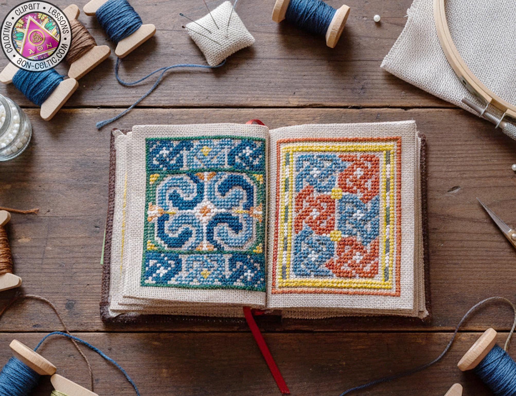 An open book with intricate cross-stitch patterns on the pages, surrounded by various crafting supplies such as spools of thread, needles, and a hoop, all arranged on a wooden surface.