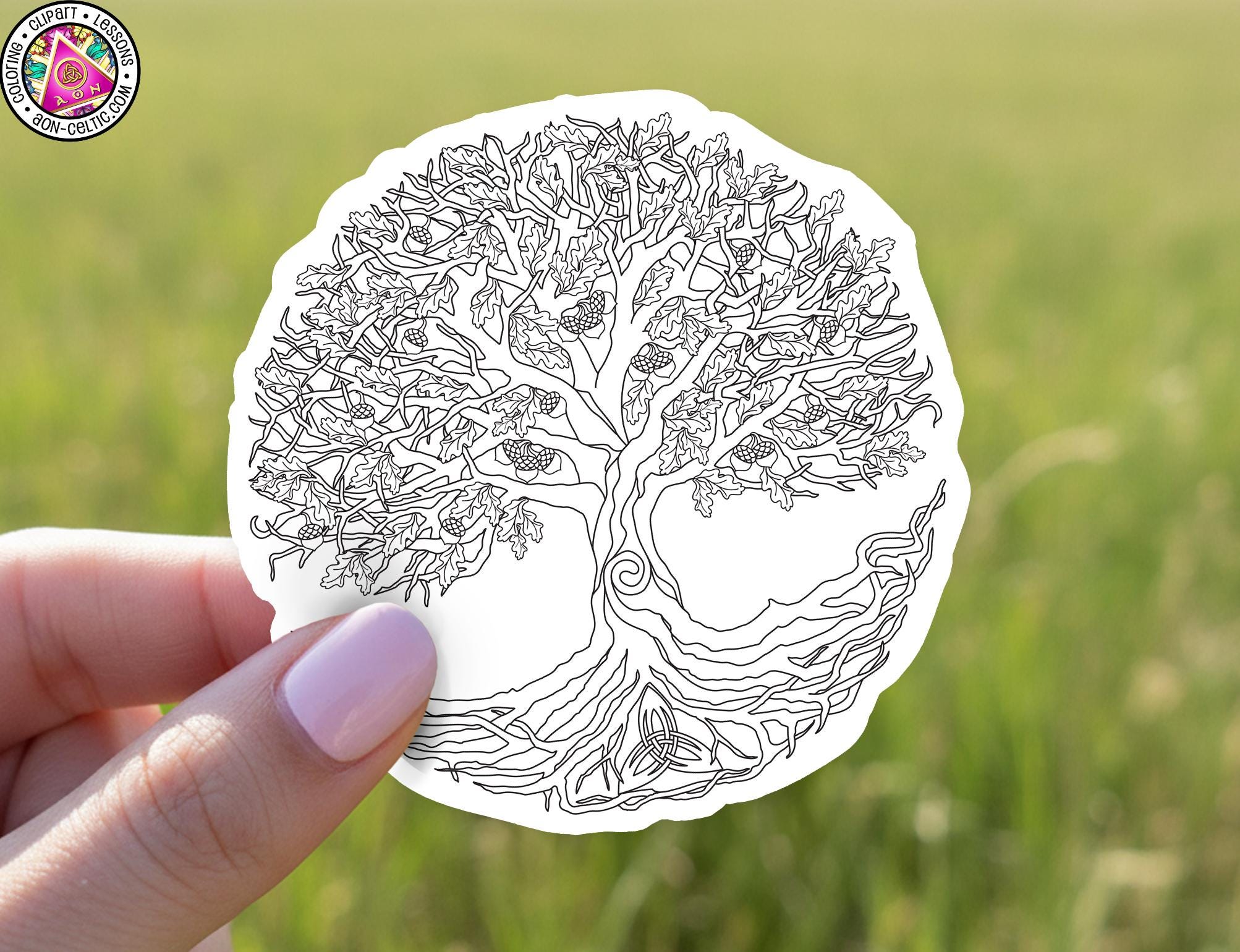 A hand holding a circular piece of paper with a detailed tree design on it, set against a blurred green field background.