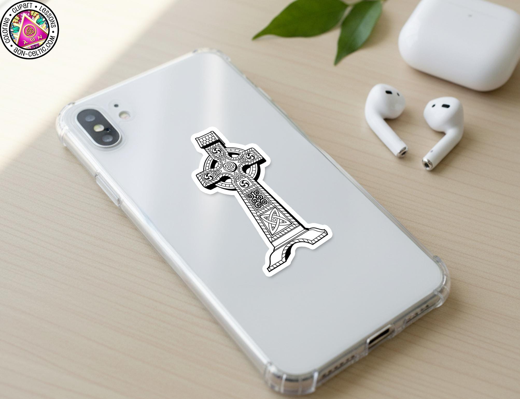 a smartphone with a sticker of a cross on its back cover, along with a pair of earbuds and a white earbud case on a wooden surface.