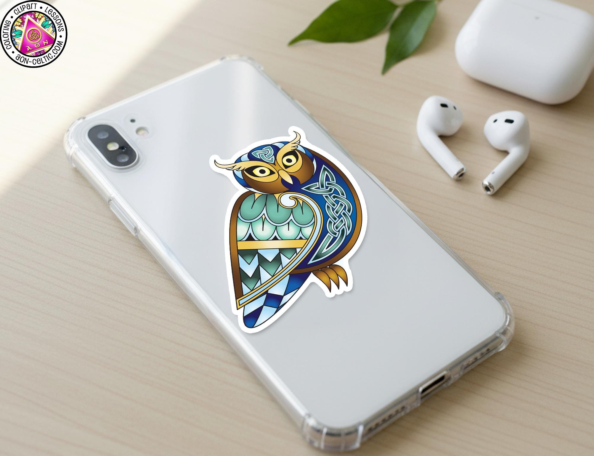 a smartphone with a colorful sticker of an owl on its back cover, along with a pair of earbuds and a white earbud case on a wooden surface.