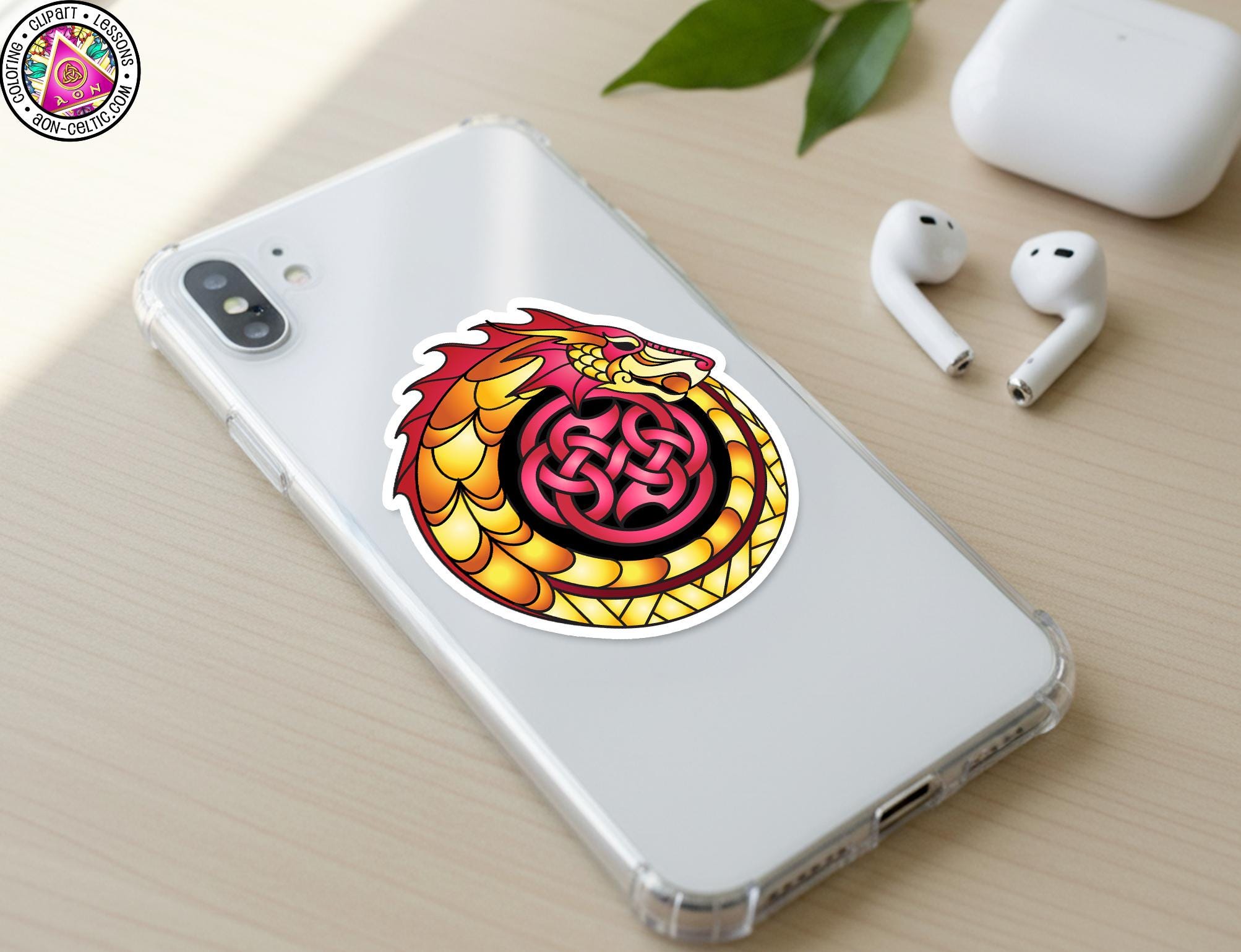 a smartphone with a sticker of a dragon design on its back cover, along with a pair of earbuds and a white earbud case on a wooden surface.