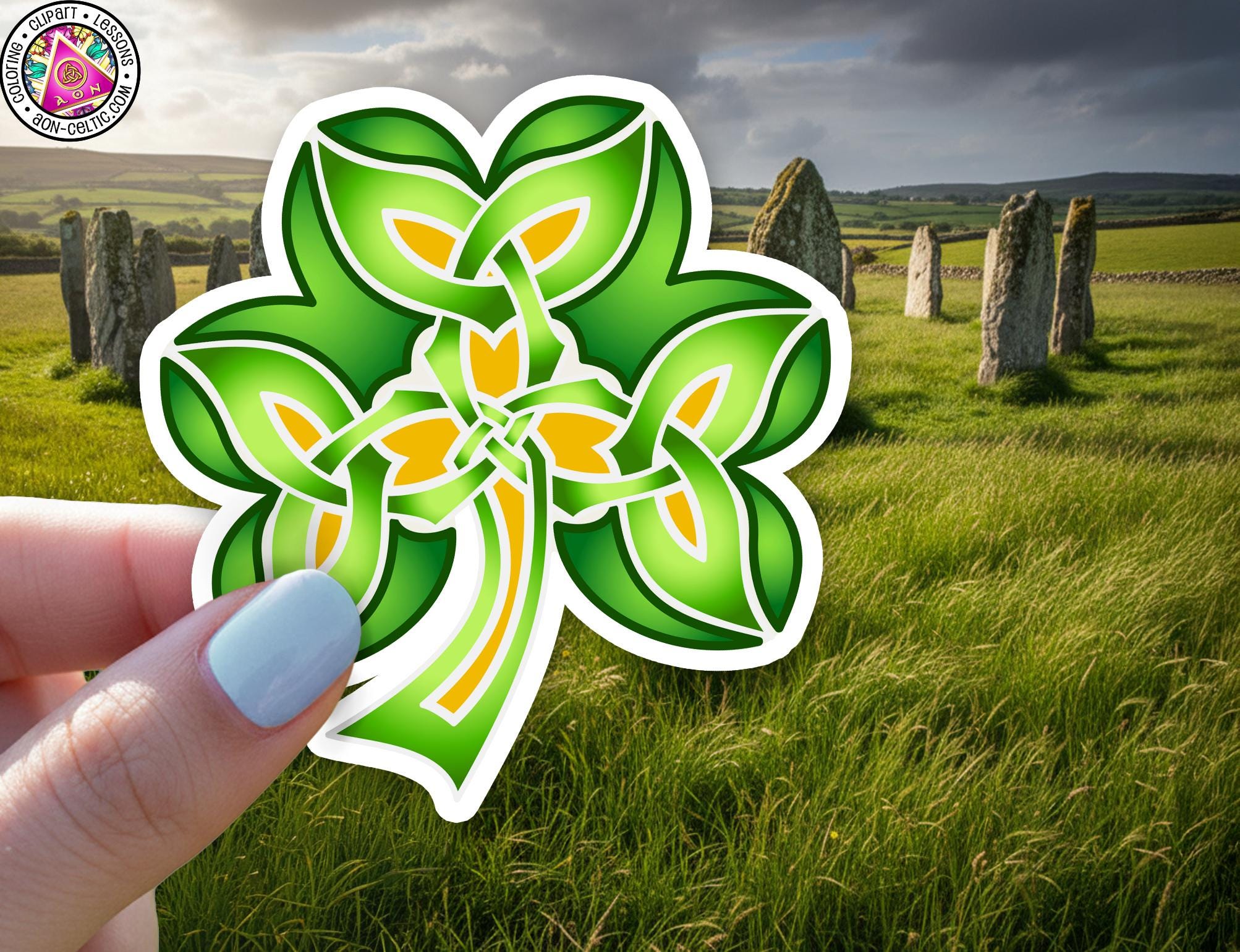 A hand holding a green and yellow clover-shaped sticker against a backdrop of a grassy field with stone markers and a cloudy sky.