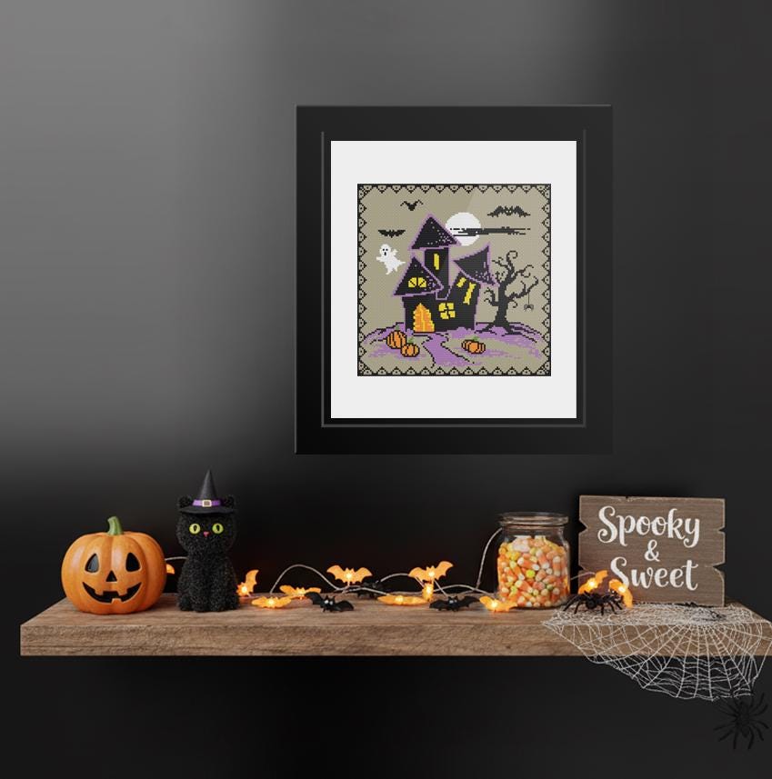 a Halloween-themed display on a shelf, including a framed picture of a spooky house, a carved pumpkin, a witch&#39;s hat, a spider web, a jar of candy, and a sign that says &quot;Spooky & Sweet&quot;.