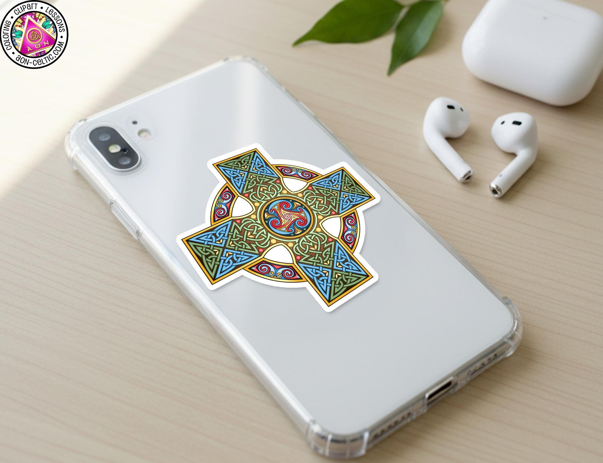 a smartphone with a colorful sticker of a Celtic cross design on its back cover, along with a pair of white earbuds and a white phone case.