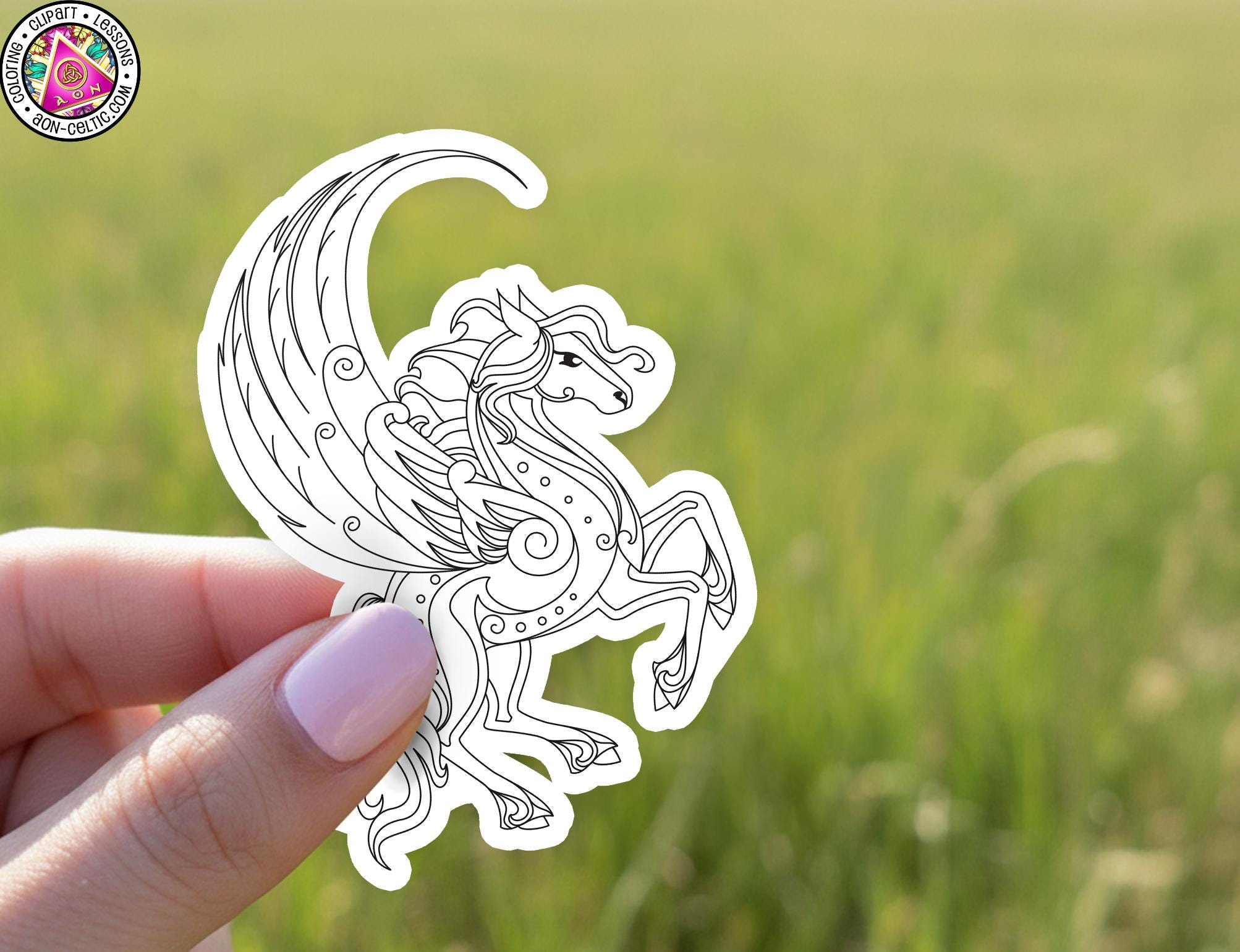 A hand holding a small, stylized illustration of a winged creature against a blurred green background.