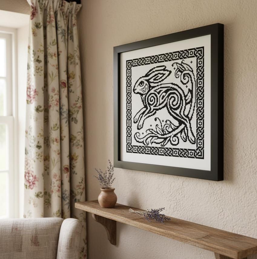 a framed artwork of a rabbit or hare, which is hanging on a wall above a wooden shelf. The shelf has a vase with purple flowers and a small plant on it. The room also has a window with floral curtains and a white sofa.