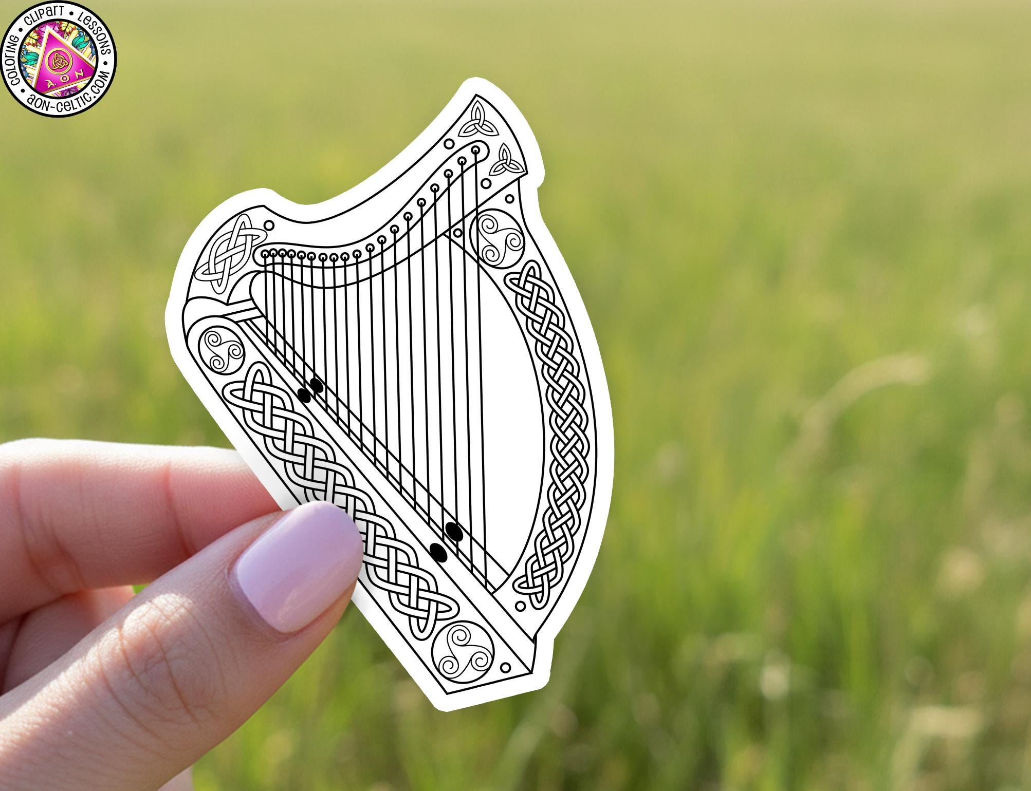 A hand holding a sticker of a harp against a blurred green background.