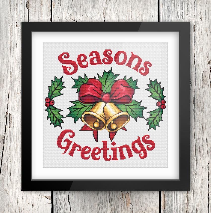 The image is a framed cross-stitch design featuring a bell, holly leaves, and the text "Seasons Greetings" in a decorative font.