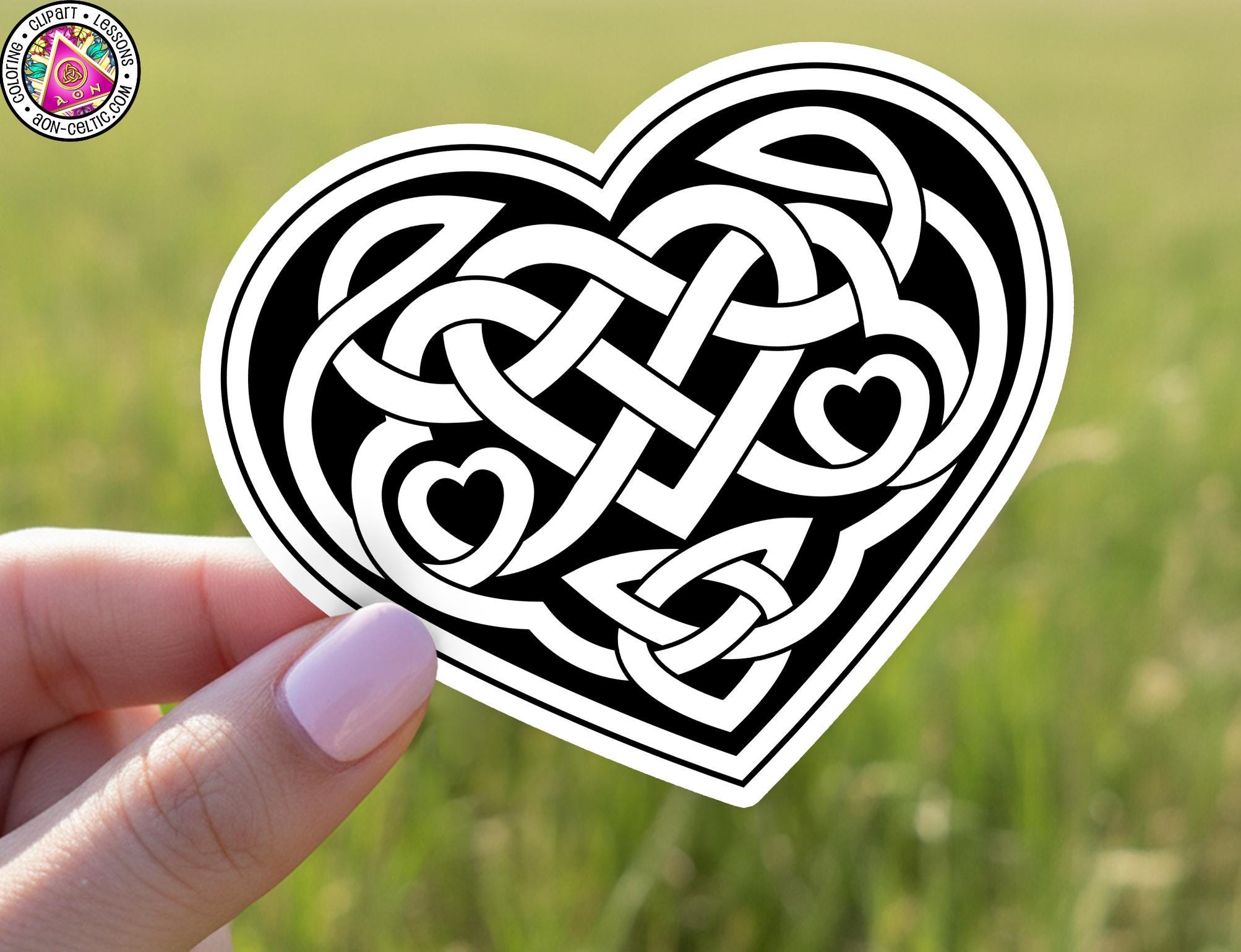 A hand holding a heart-shaped sticker with a Celtic knot design.