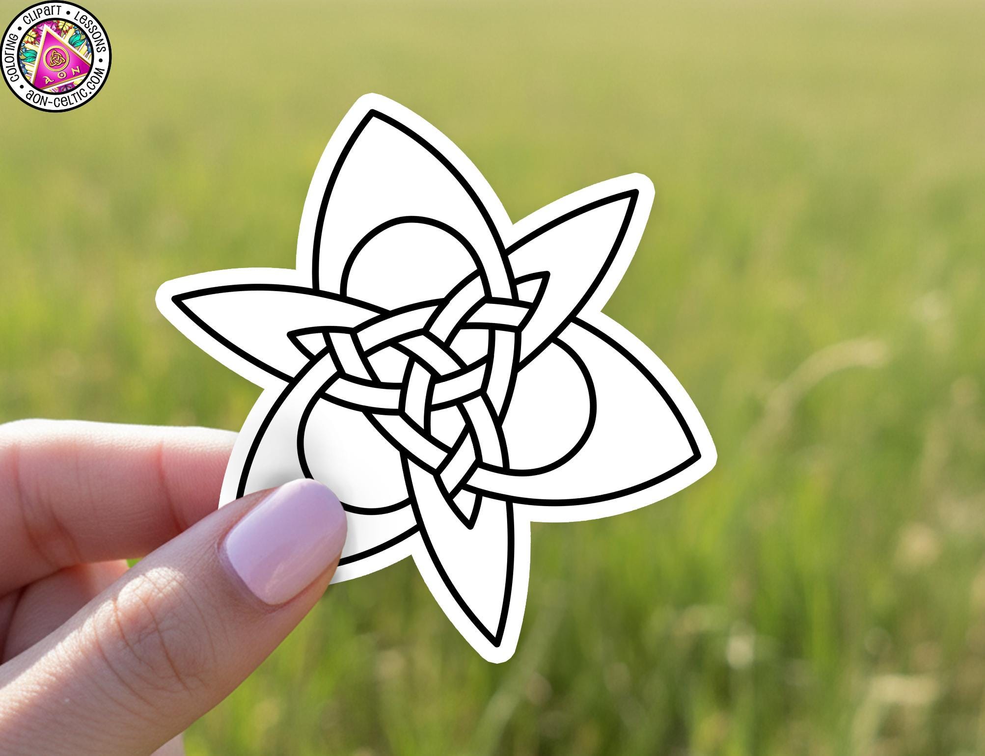 A hand holding a sticker with a black and white design resembling a flower or plant.