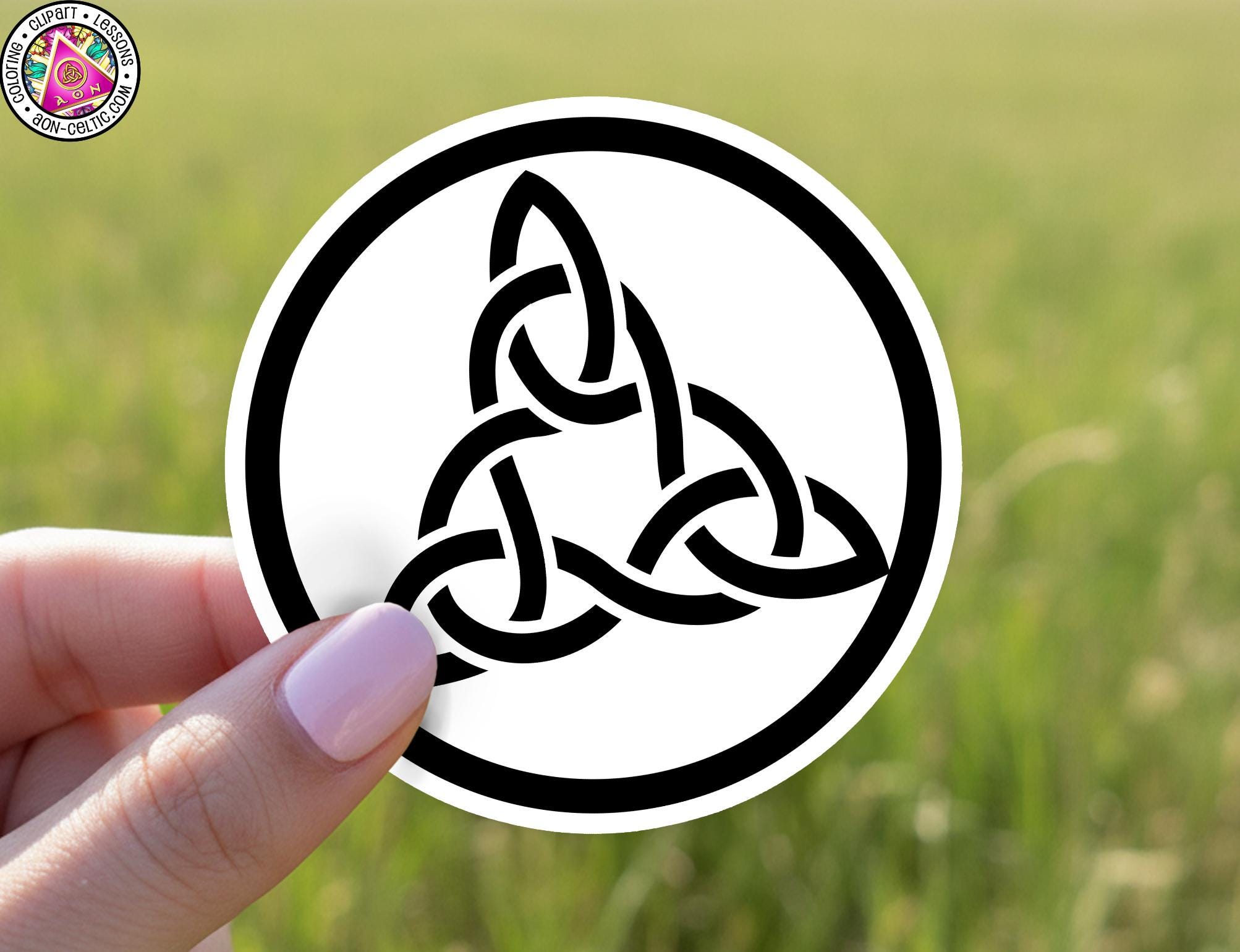 A hand holding a circular sticker with a black and white design of a Celtic knot.