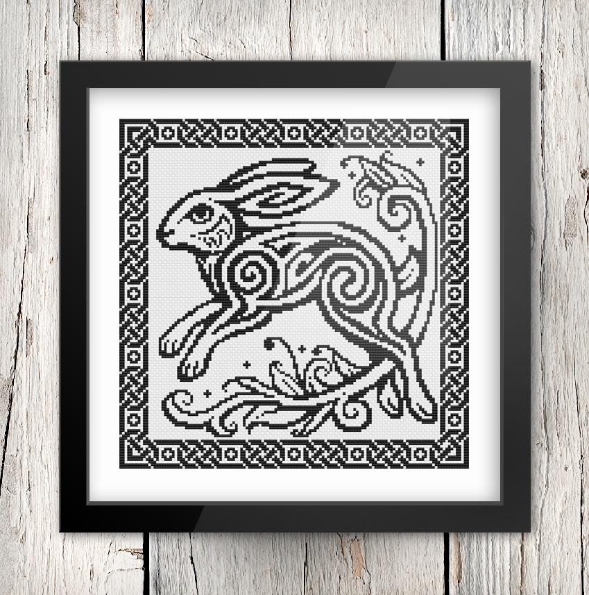 The image is a framed cross-stitch design featuring a stylized rabbit or hare with intricate swirling patterns.