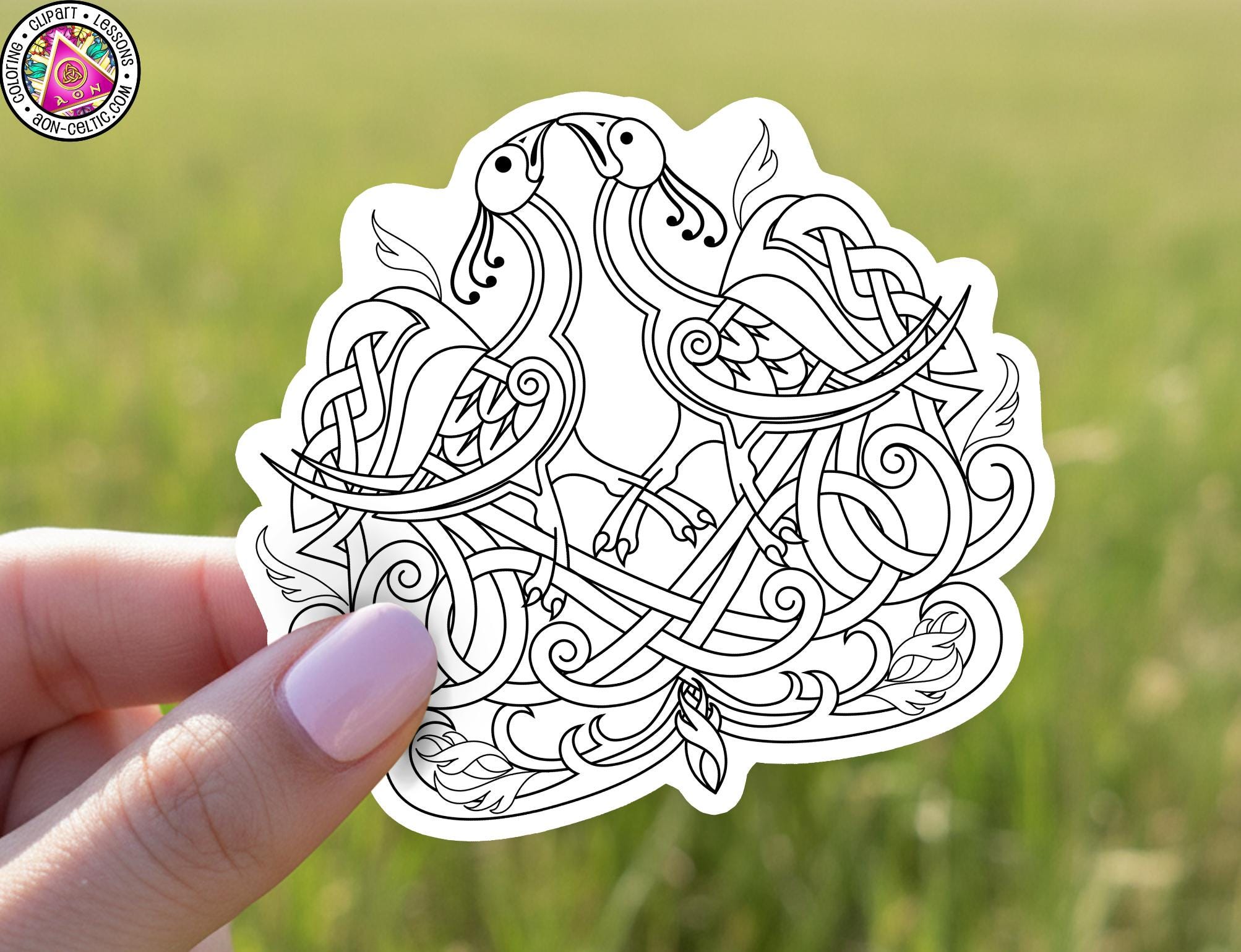 A hand holding a sticker with an intricate, hand-drawn design featuring two stylized birds or creatures.