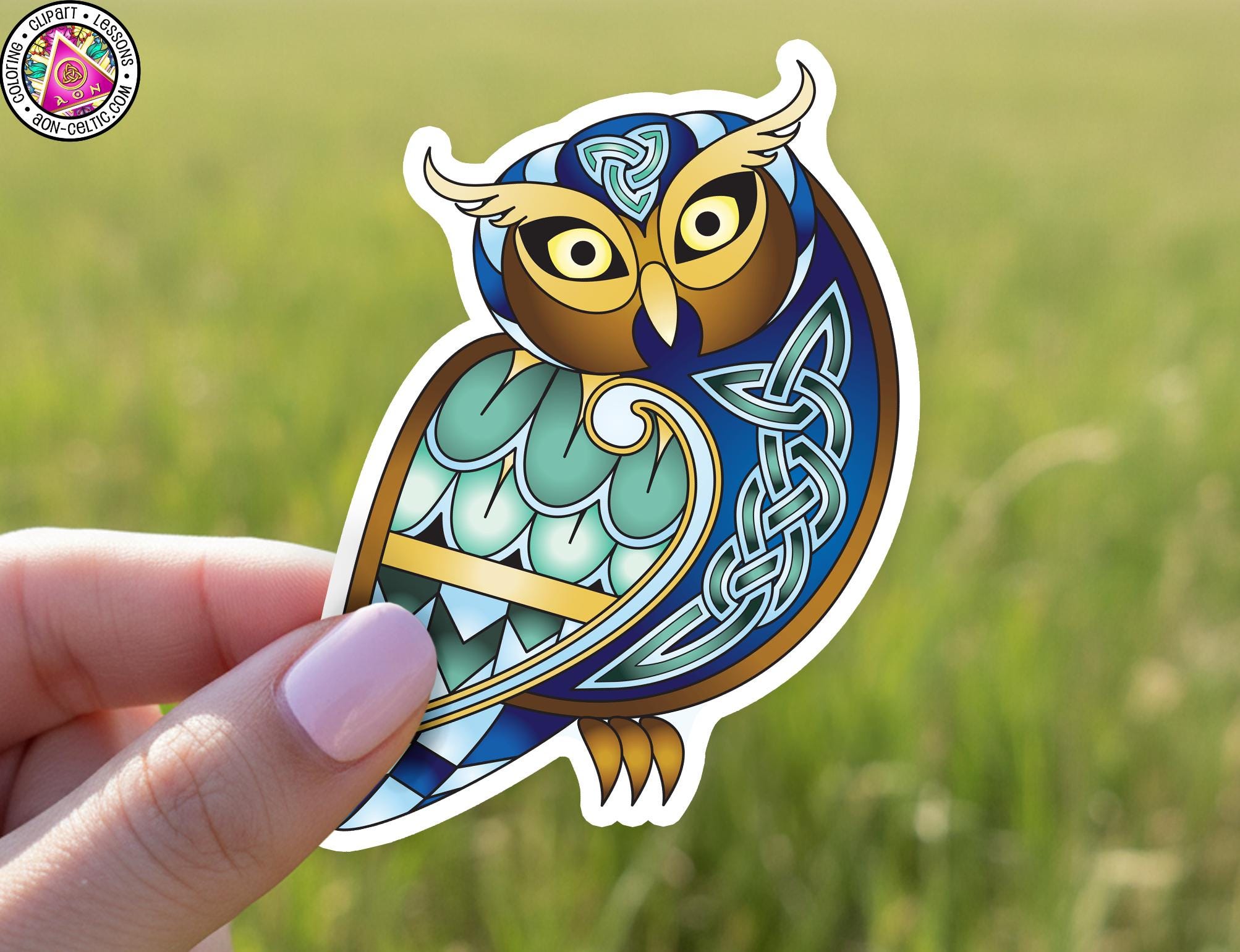 A hand holding a sticker of an ornate owl with intricate designs and patterns.