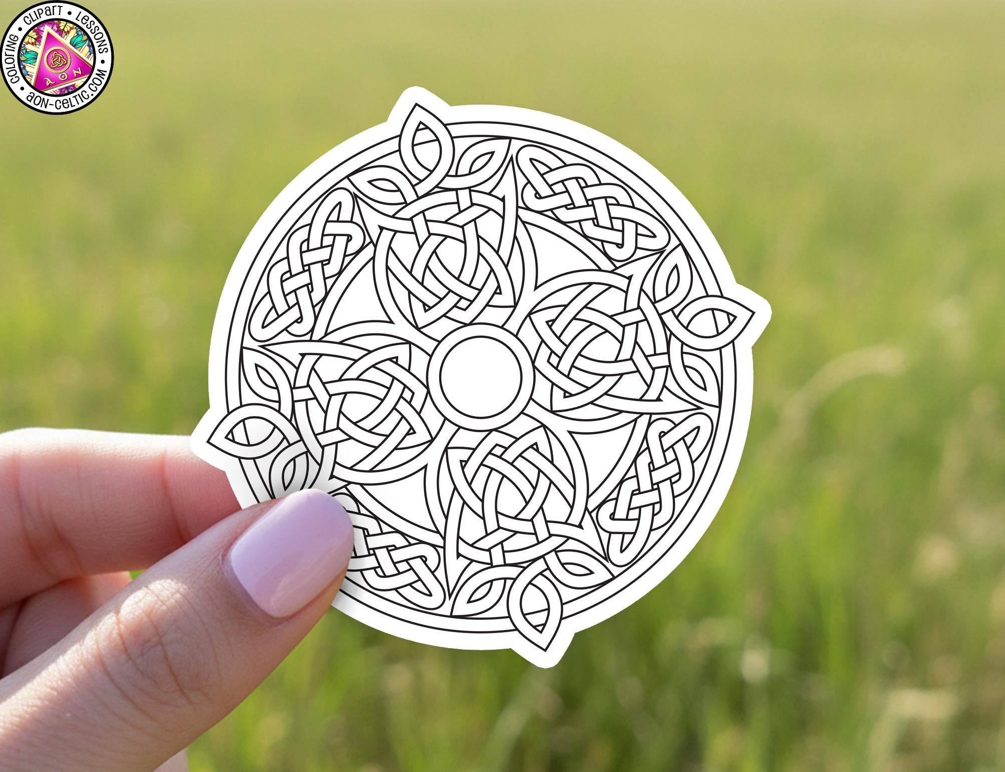 A hand holding a circular sticker with an intricate Celtic knot design.
