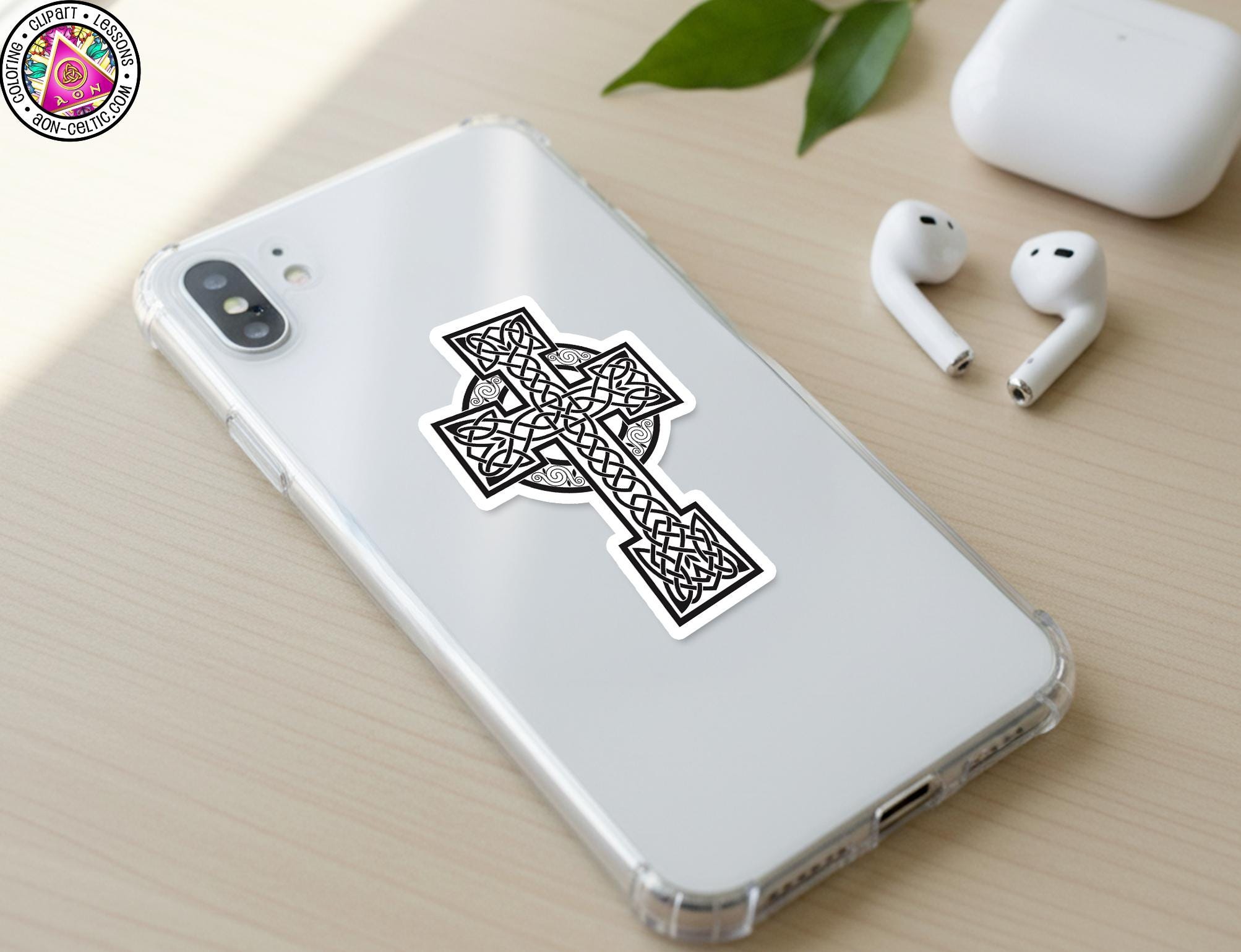 a white smartphone with a sticker of a Celtic cross on its back cover, along with a pair of white earbuds and a white charging cable on a wooden surface.
