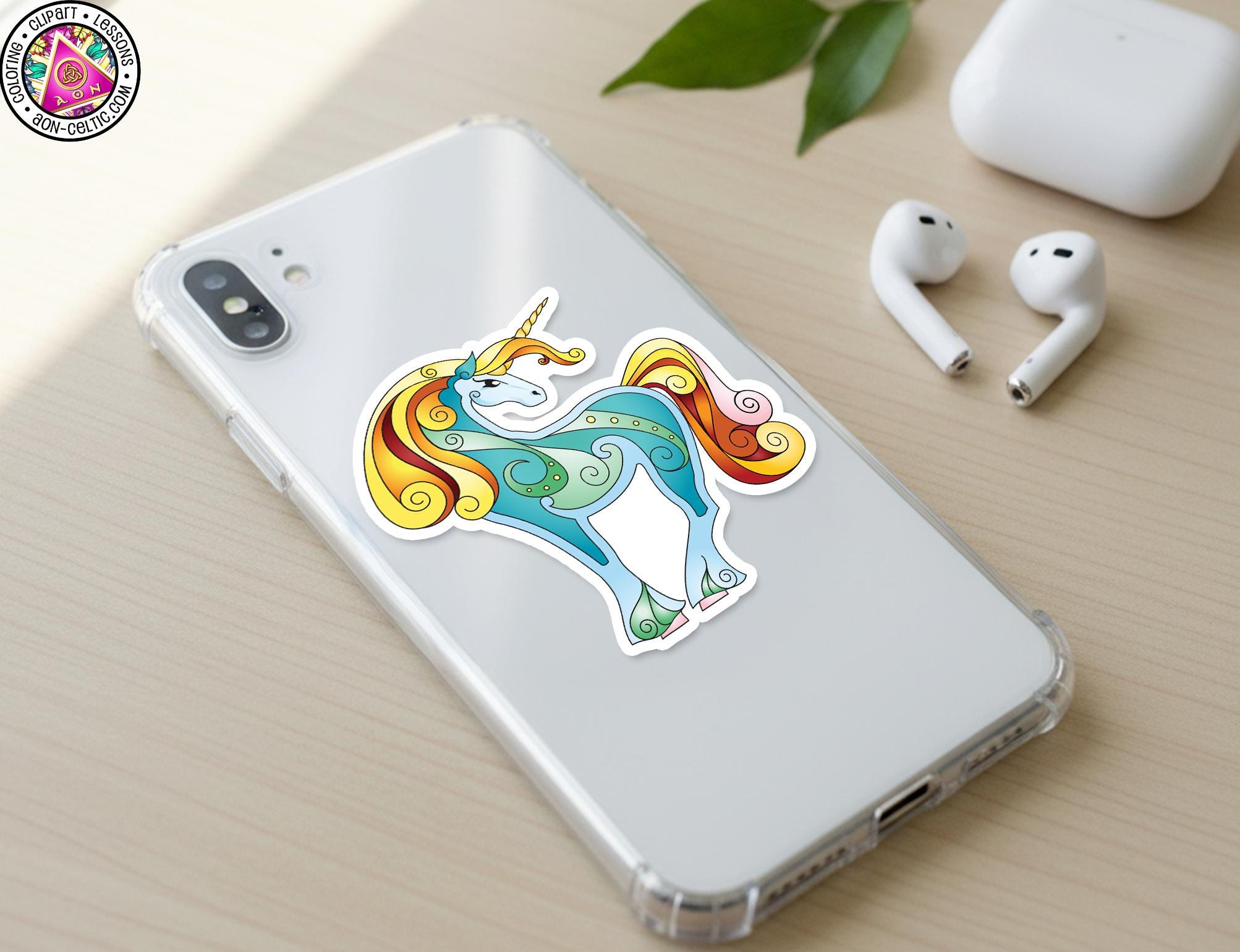 a smartphone with a colorful sticker of a unicorn on its back cover, along with a pair of earbuds and a white earbud case on a wooden surface.