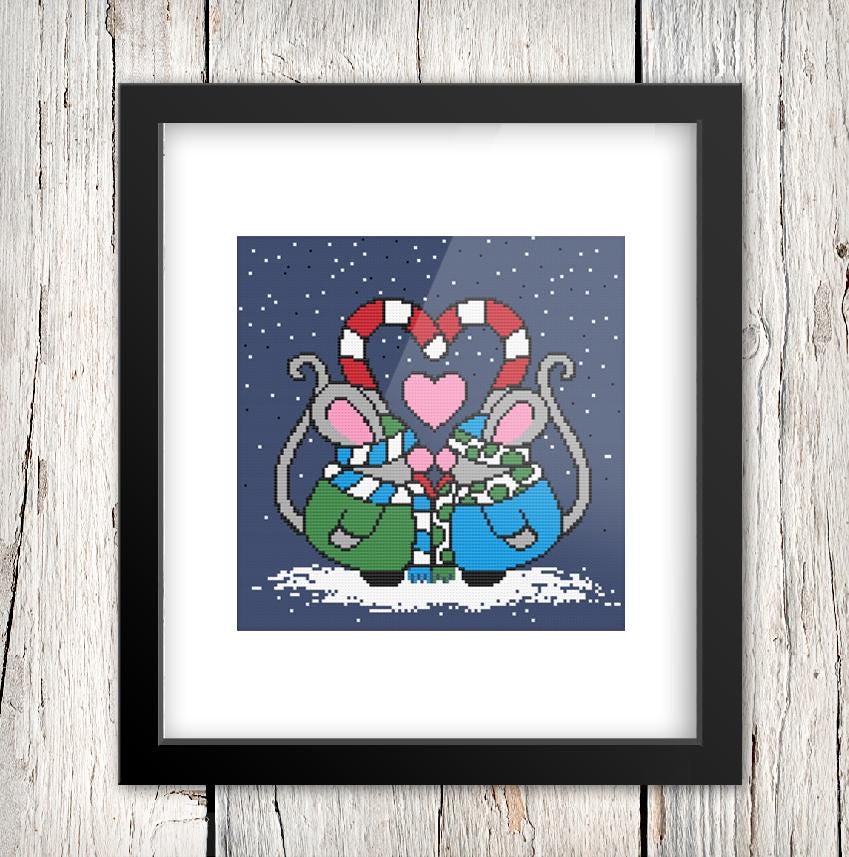 A framed cross-stitch image depicting two mice in a snowy winter scene, with a heart-shaped candy cane and snowflakes in the background.