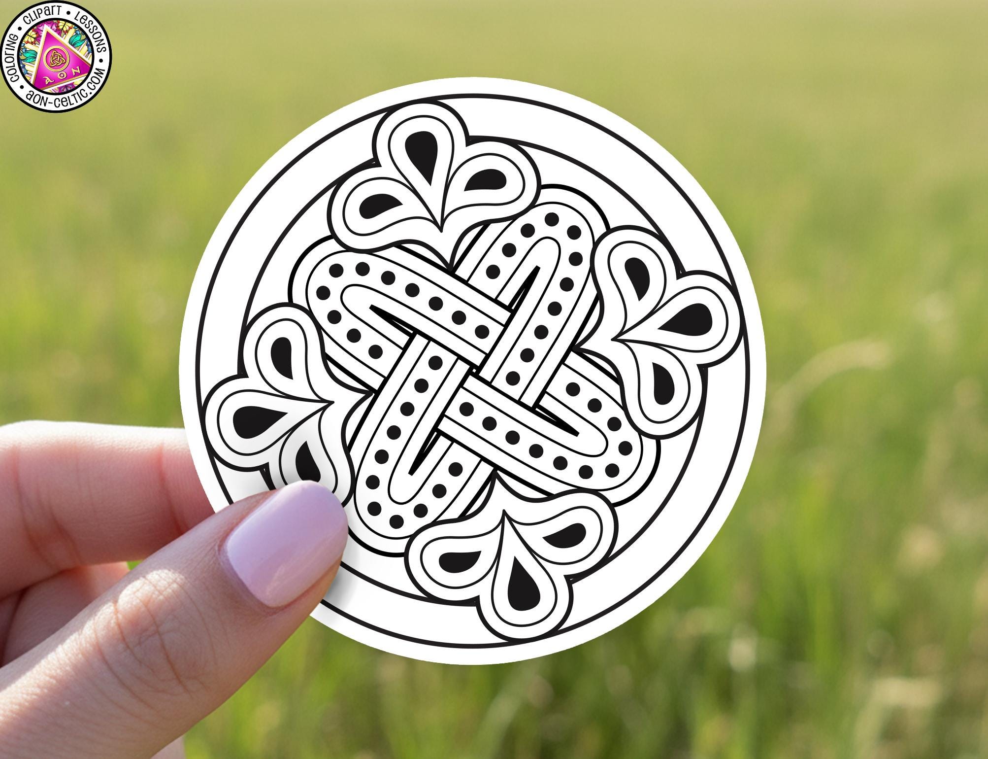 A hand holding a circular sticker with a black and white design featuring a floral pattern.