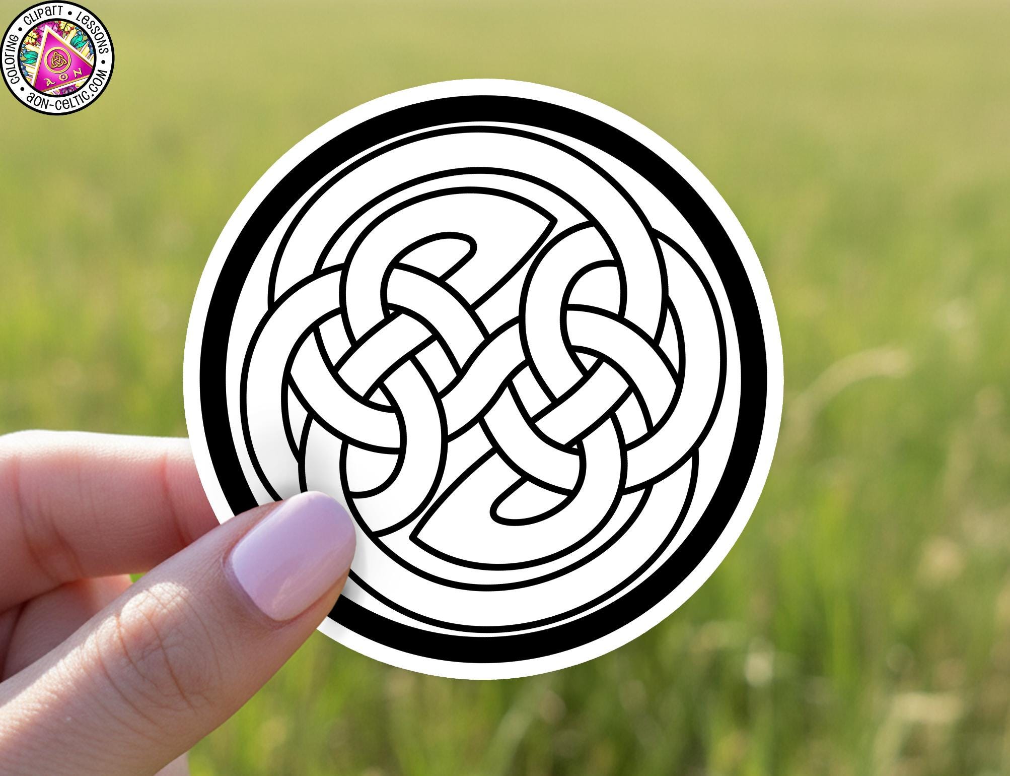 A hand holding a circular sticker with a black and white design featuring a Celtic knot pattern.