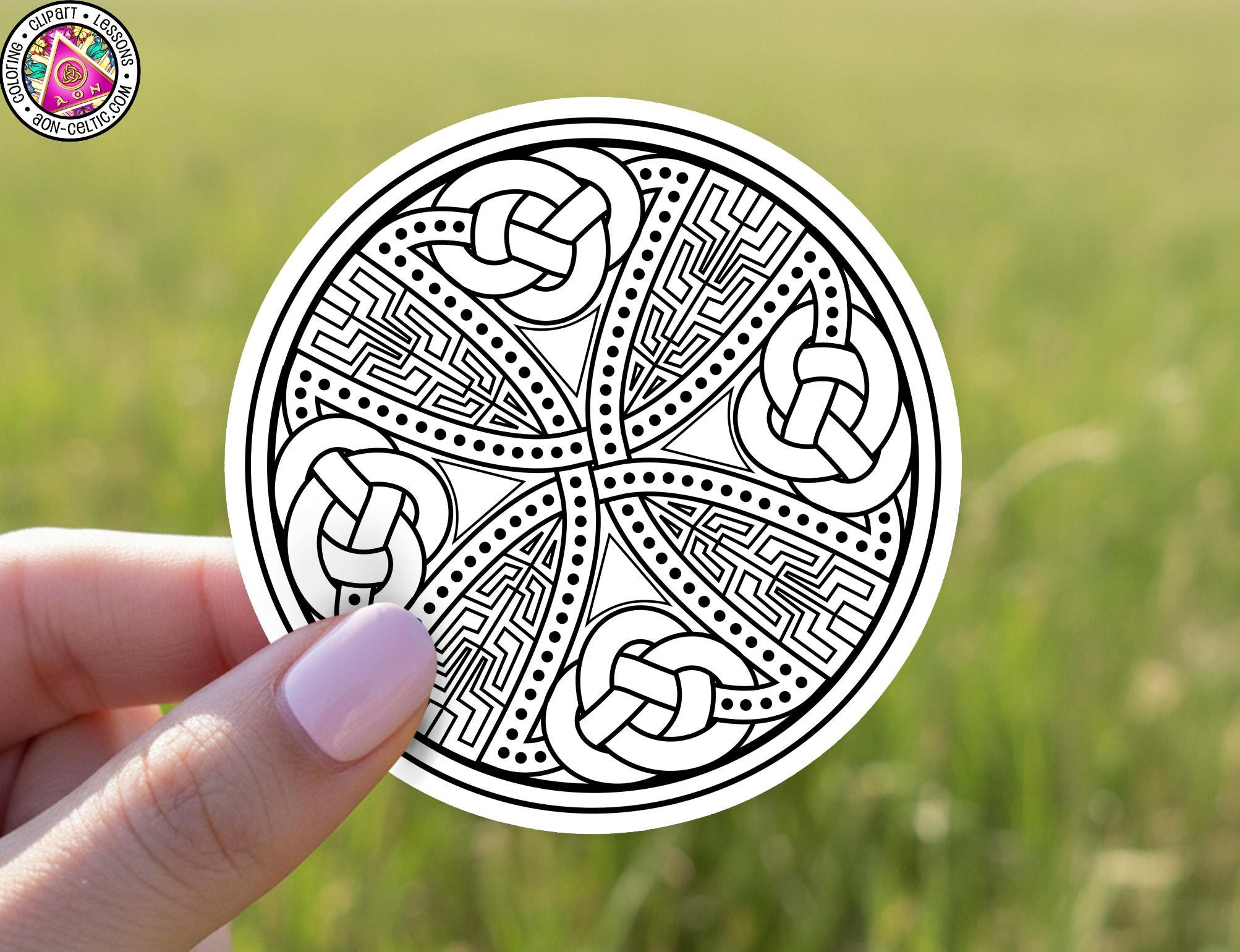 A hand holding a circular sticker with an intricate, abstract design featuring various shapes and patterns.