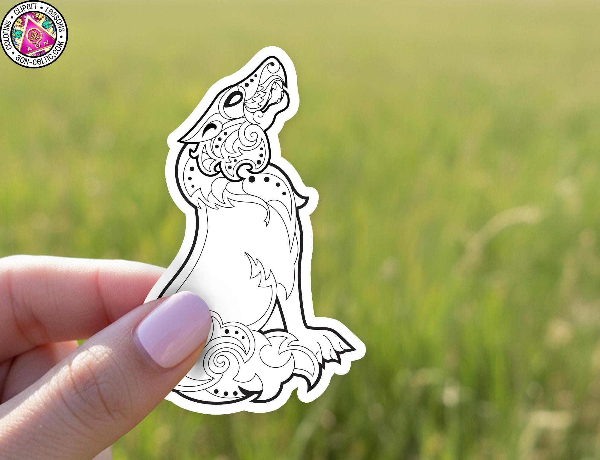 A hand holding a sticker of a stylized wolf or wolf-like creature against a blurred green background.