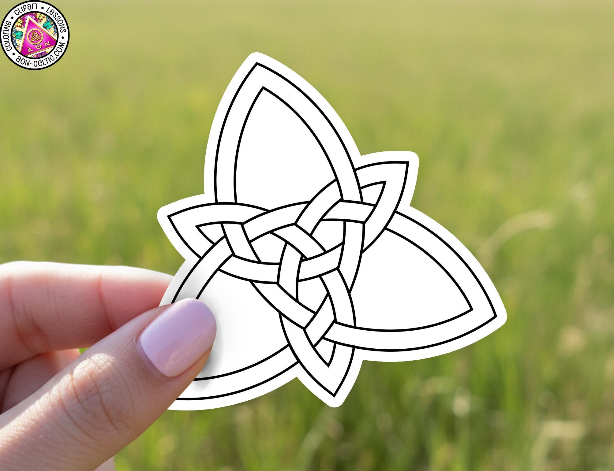A hand holding a sticker with a geometric design, against a blurred green background.